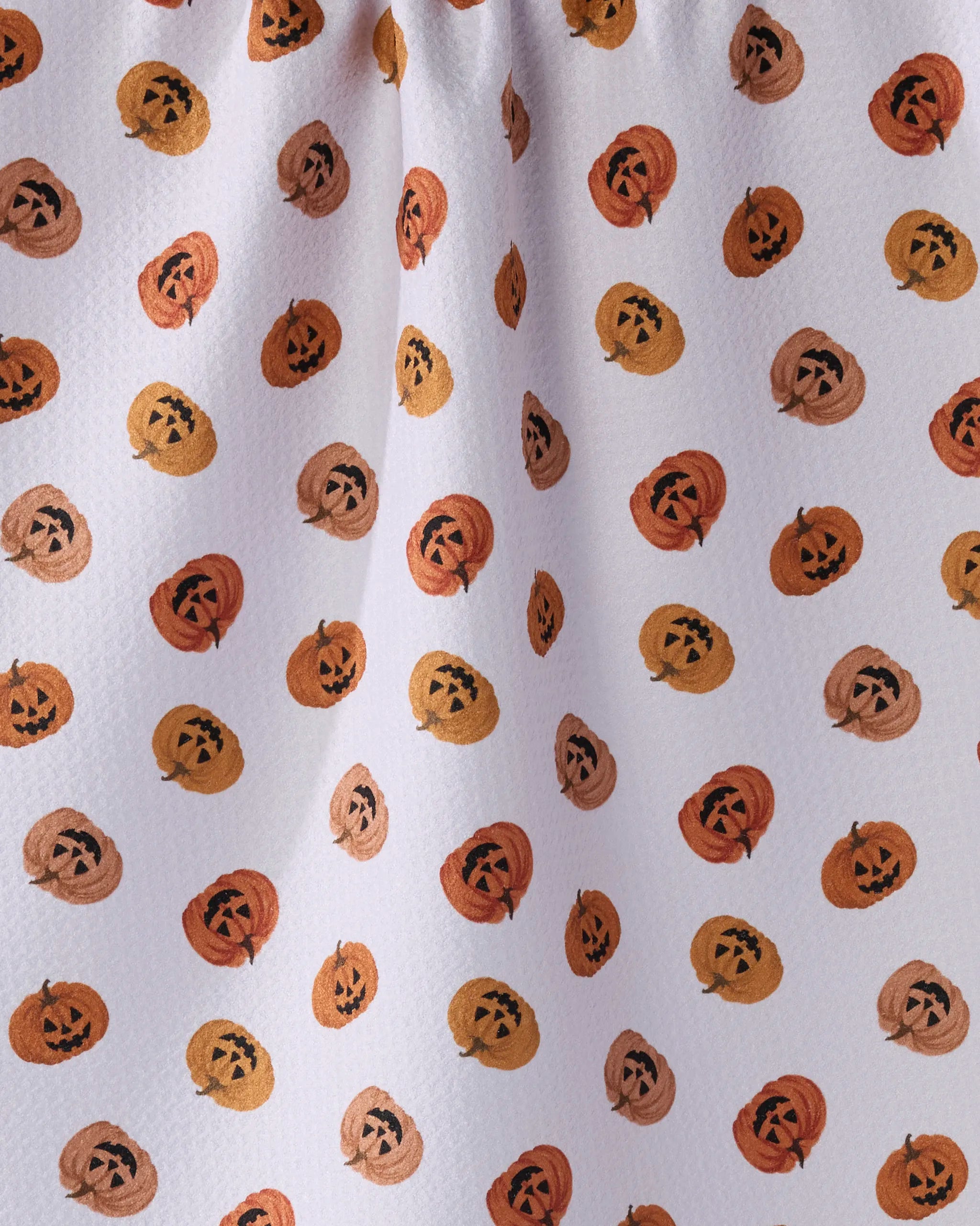 The Geometry Jacks Parade tea towel features an ultra-absorbent white fabric with a repeating pattern of orange, brown, and beige jack-o-lanterns, each displaying unique smiling faces and triangular eyes.