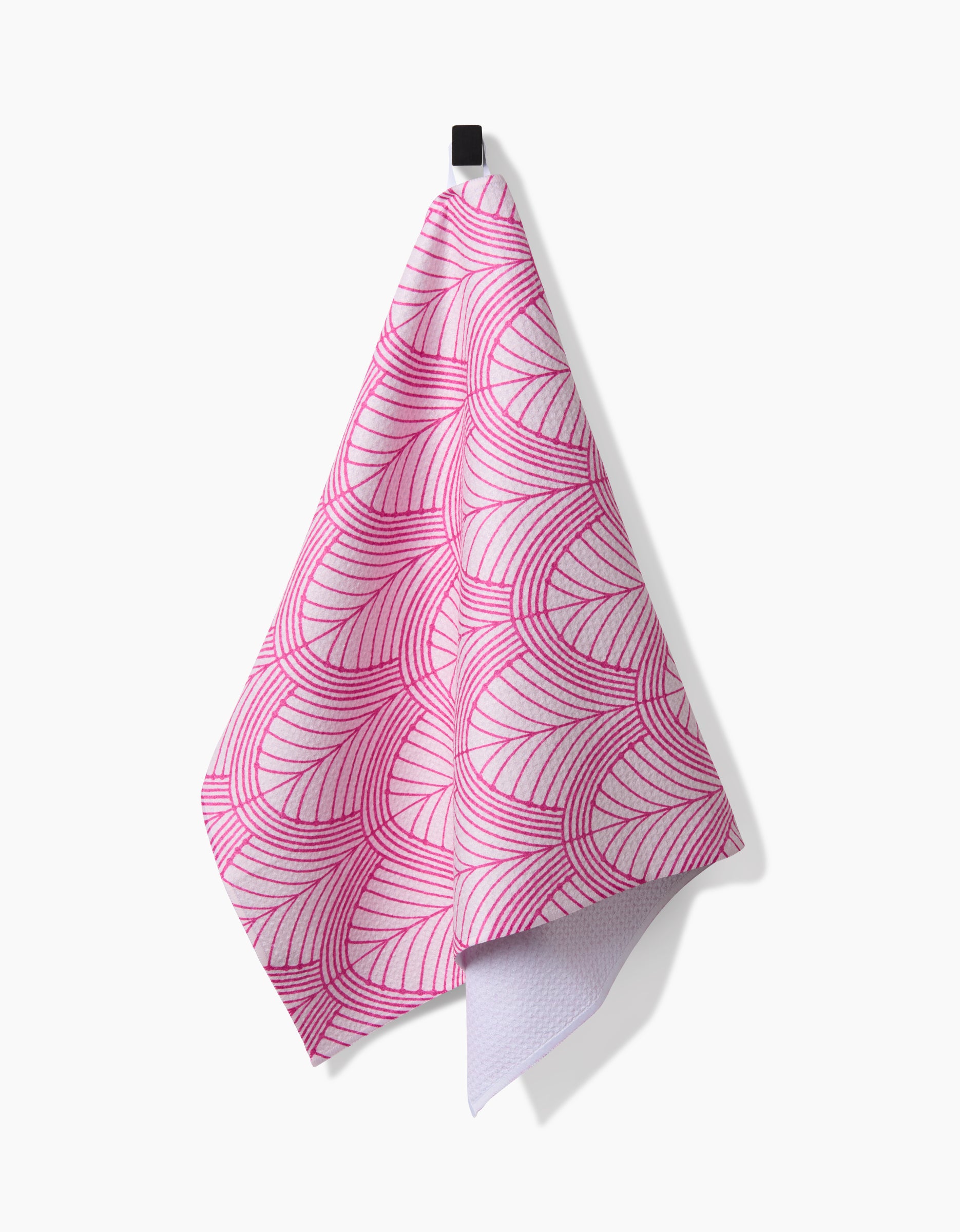 The Amy MacCready Jaskin Tea Towel in white features a pink geometric wave design and hangs from a black hook. Made from Geoweave fabric, it blends contemporary style with functionality for your modern kitchen.