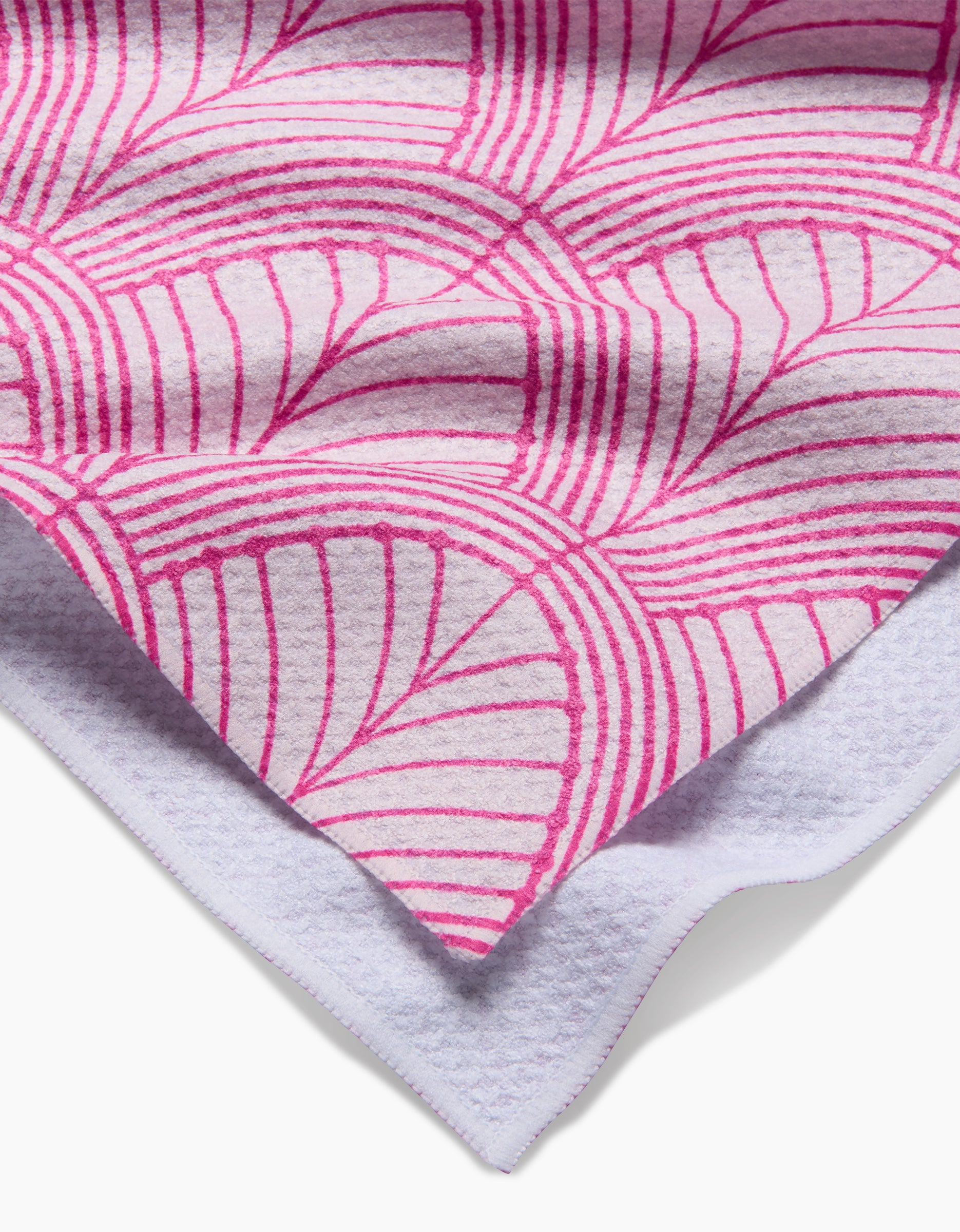 A close-up of the Amy MacCready Jaskin Tea Towel, showcasing its white background, bold pink geometric design, and textured white Geoweave fabric underside, folded at the corner.