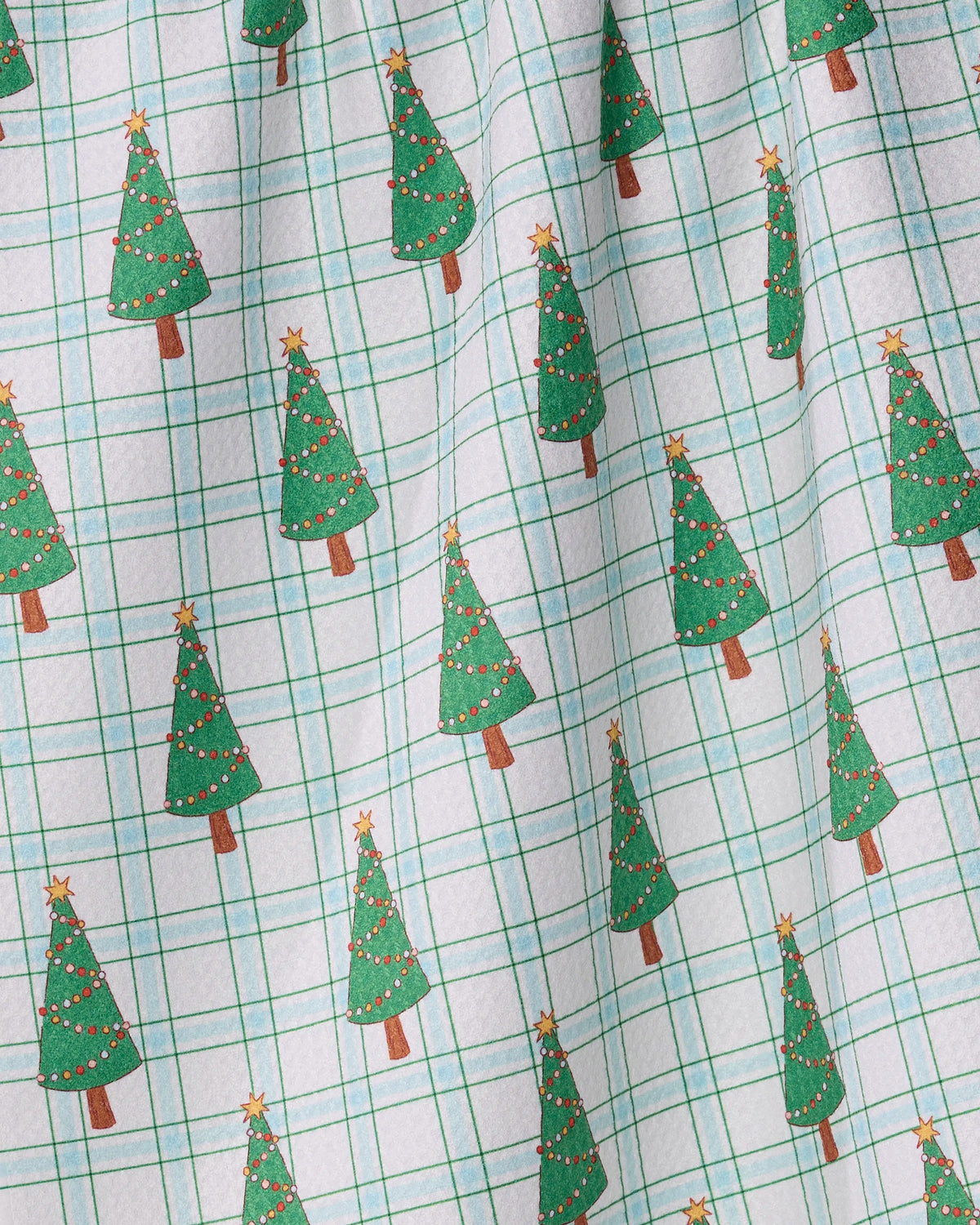 The Jolly Plaid kitchen tea towel by Geometry features a white fabric with a light blue and green plaid design, accented by evenly spaced green Christmas trees adorned with ornaments and topped with stars. Crafted from recycled materials, this slightly wrinkled towel brings a cozy, festive charm to any space.