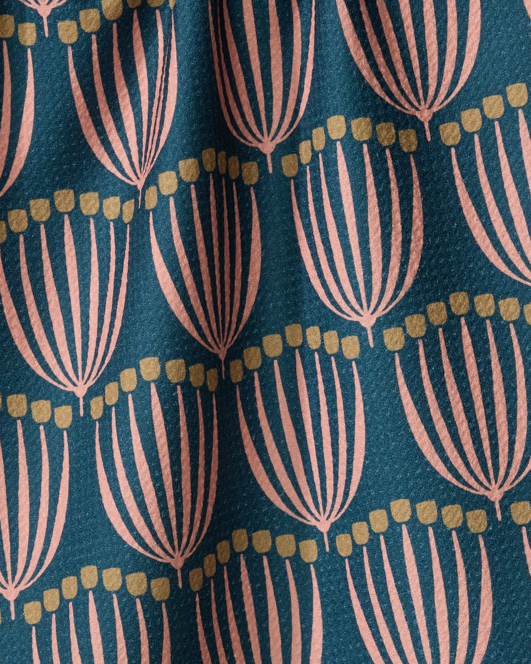 A close-up of the Josie tea towel by Amy MacCready shows its eco-friendly, textured fabric with stylized pink flowers and yellow dots on dark teal. Gentle folds in the towel add to its cozy, inviting look.