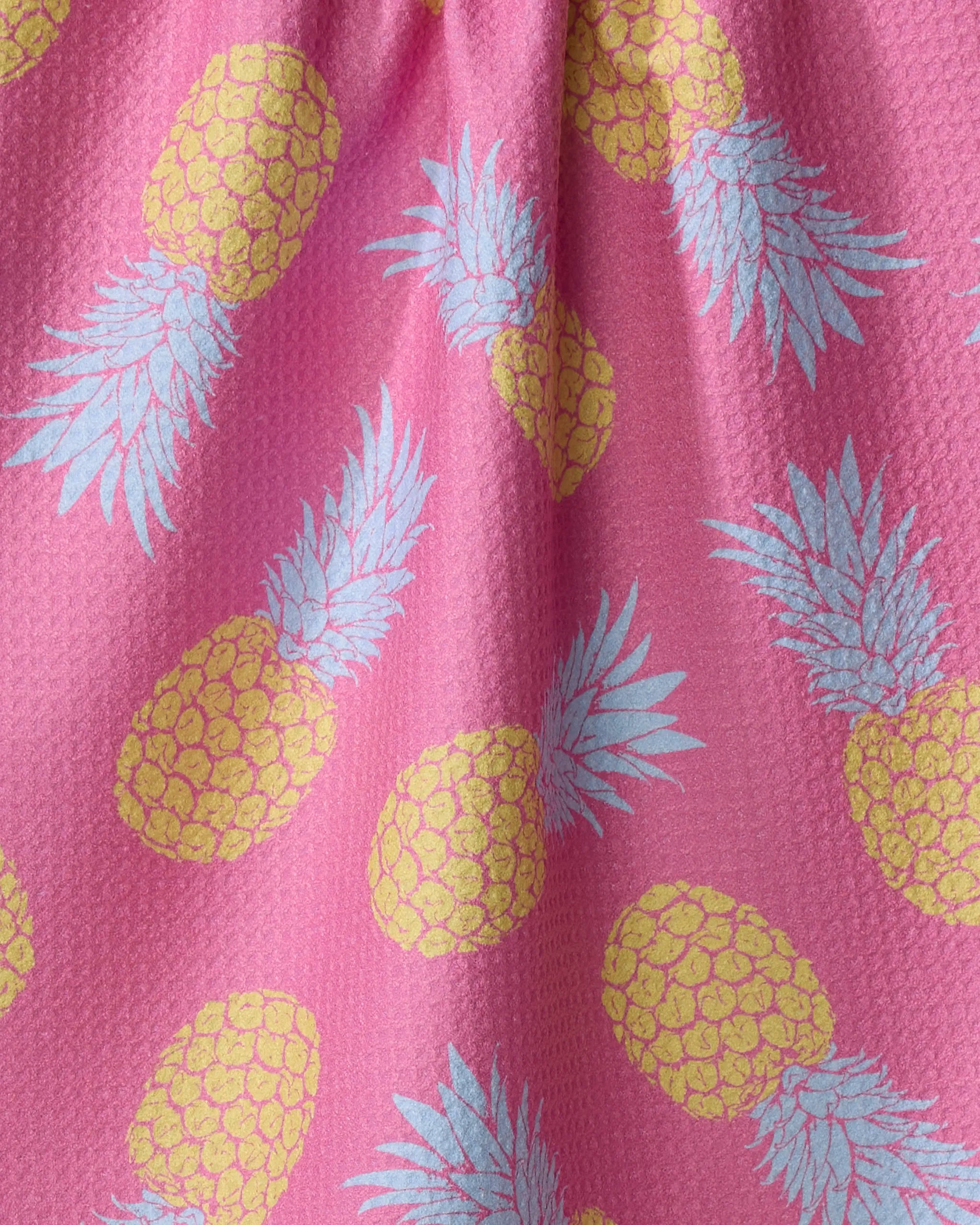 Close-up of the Juicy Pineapples tea towel by Ashley Celena, showcasing its textured pink fabric and a repeating pattern of yellow pineapples with light blue leaves.