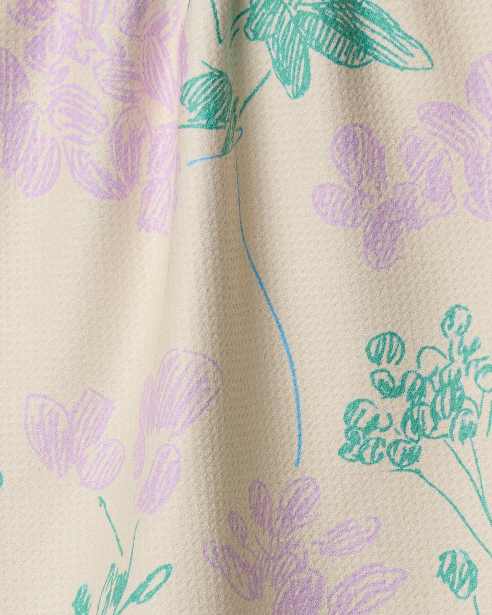 A close-up of the Geometry Julieta tea towel showcases its cream color and textured, quick-drying surface, adorned with hand-drawn floral patterns in pastel green, purple, and blue.