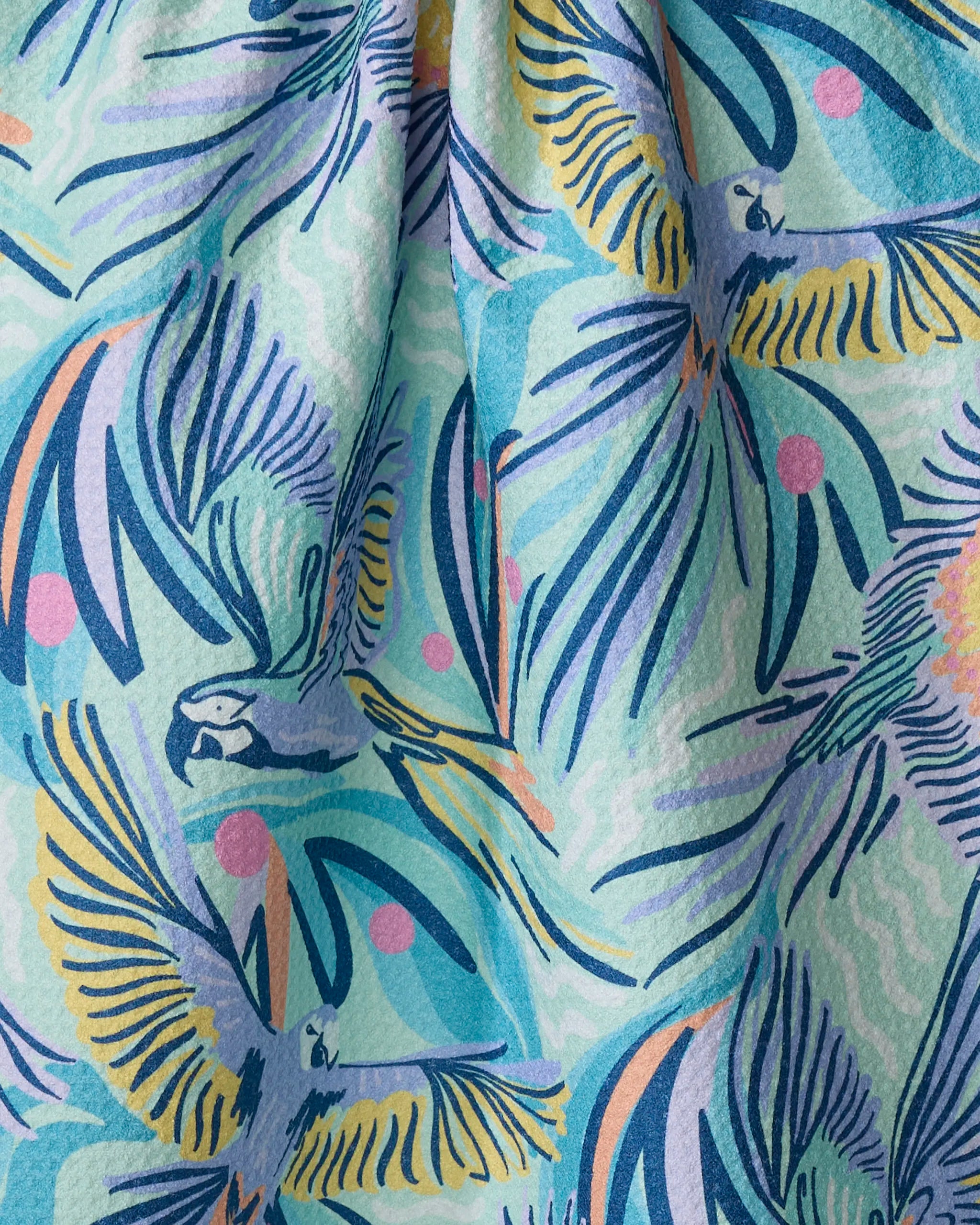 The Jungle Birds tea towel by Masha Volnova features illustrated parrots in flight among abstract blue, yellow, pink, and green tropical leaves. Its slightly textured fabric drapes beautifully for a unique kitchen accent.