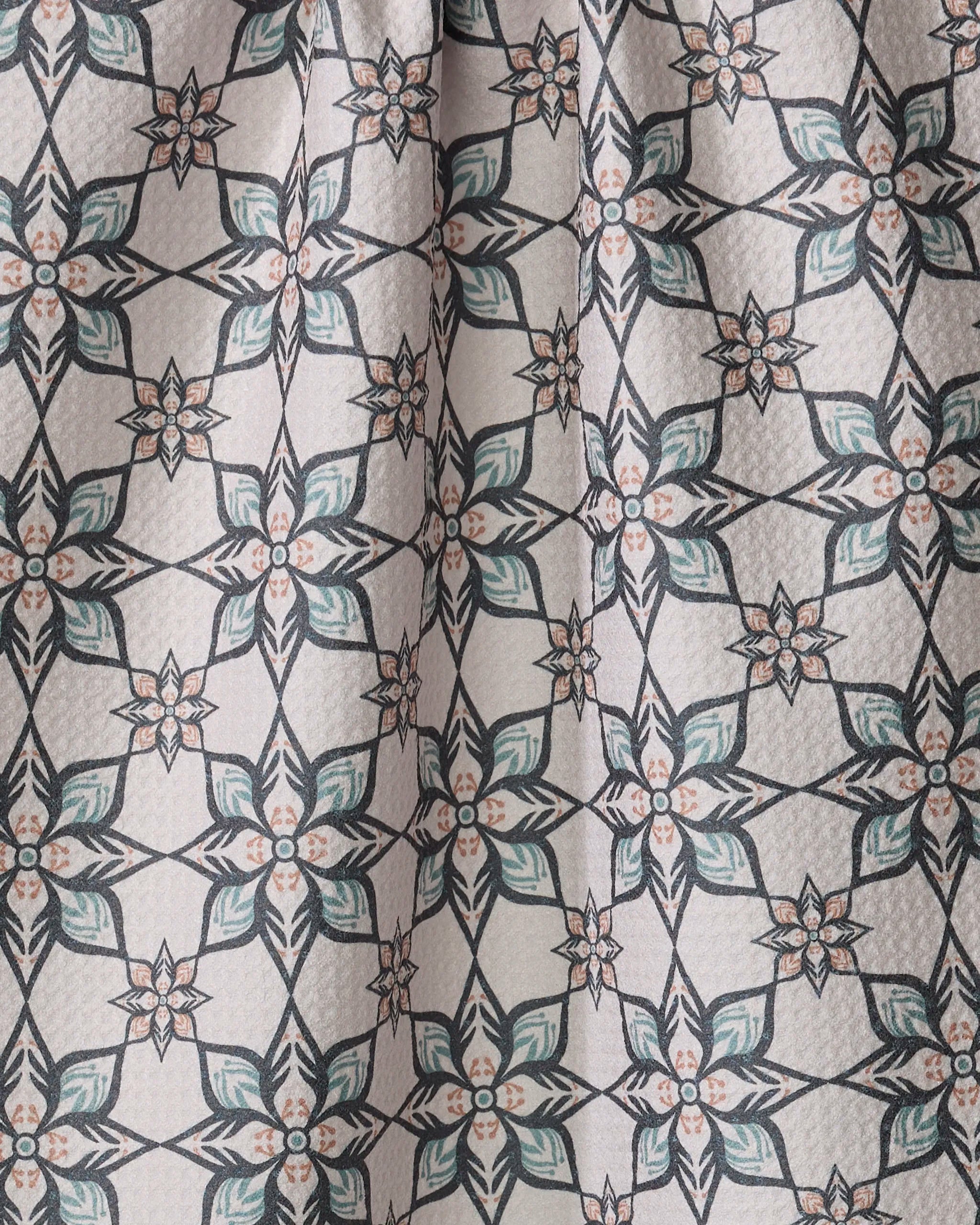 Close-up of Jungle Night dish towel by Amita Nair, showcasing absorbent fabric with a geometric floral pattern in teal, peach, and black. Repeated six-petal flowers form a symmetrical grid on a light background.