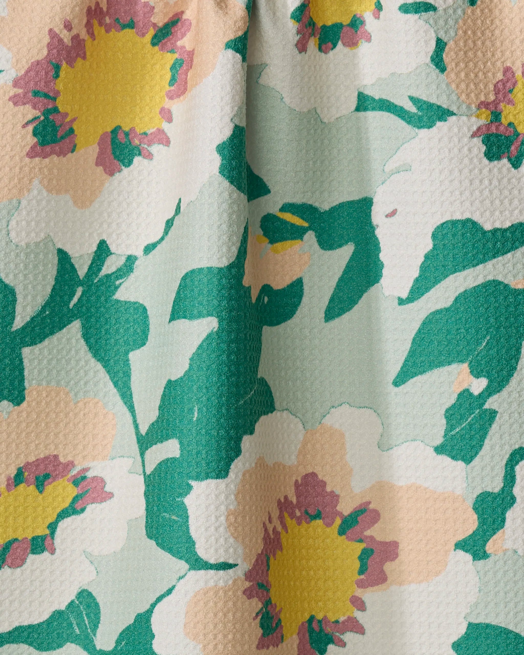 The Junie by Geometry features large abstract yellow, pink, and white flowers with green leaves on a textured light green background. This absorbent dish towel has a slightly gathered top for added style.