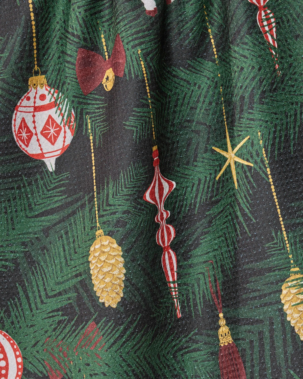 Close-up of Keepsake, an ultra-absorbent tea towel by Geometry, featuring a green pine branch pattern adorned with red, gold, and white Christmas ornaments—baubles, bows, stars, pinecones, and icicle-shaped accents—beautifully crafted from recycled materials for festive holiday cheer.