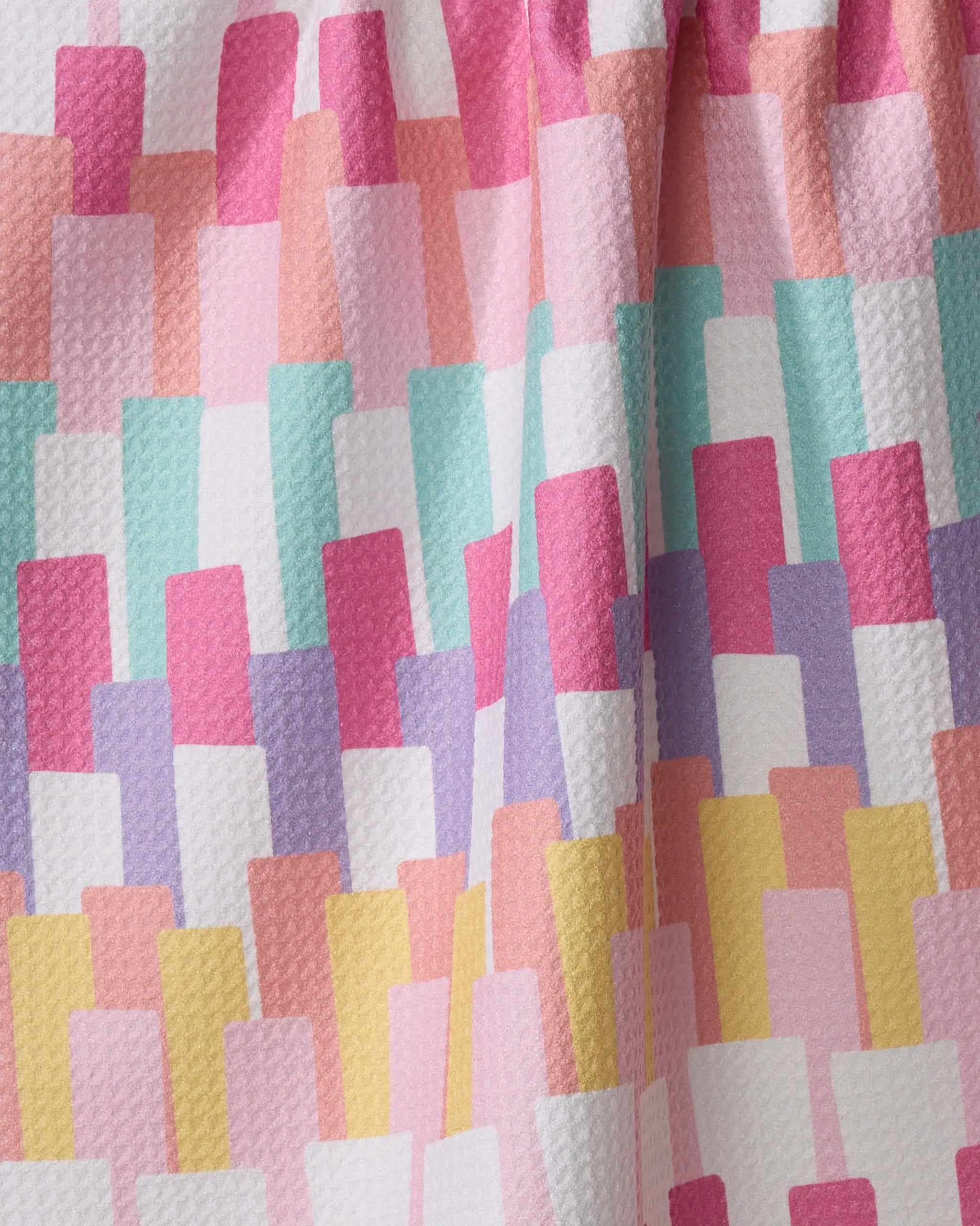 A close-up of the "Keys" kitchen towel by Rebecca Bobko, made from recycled materials and featuring a geometric pattern of overlapping rectangles in pastel pink, peach, purple, teal, and white.