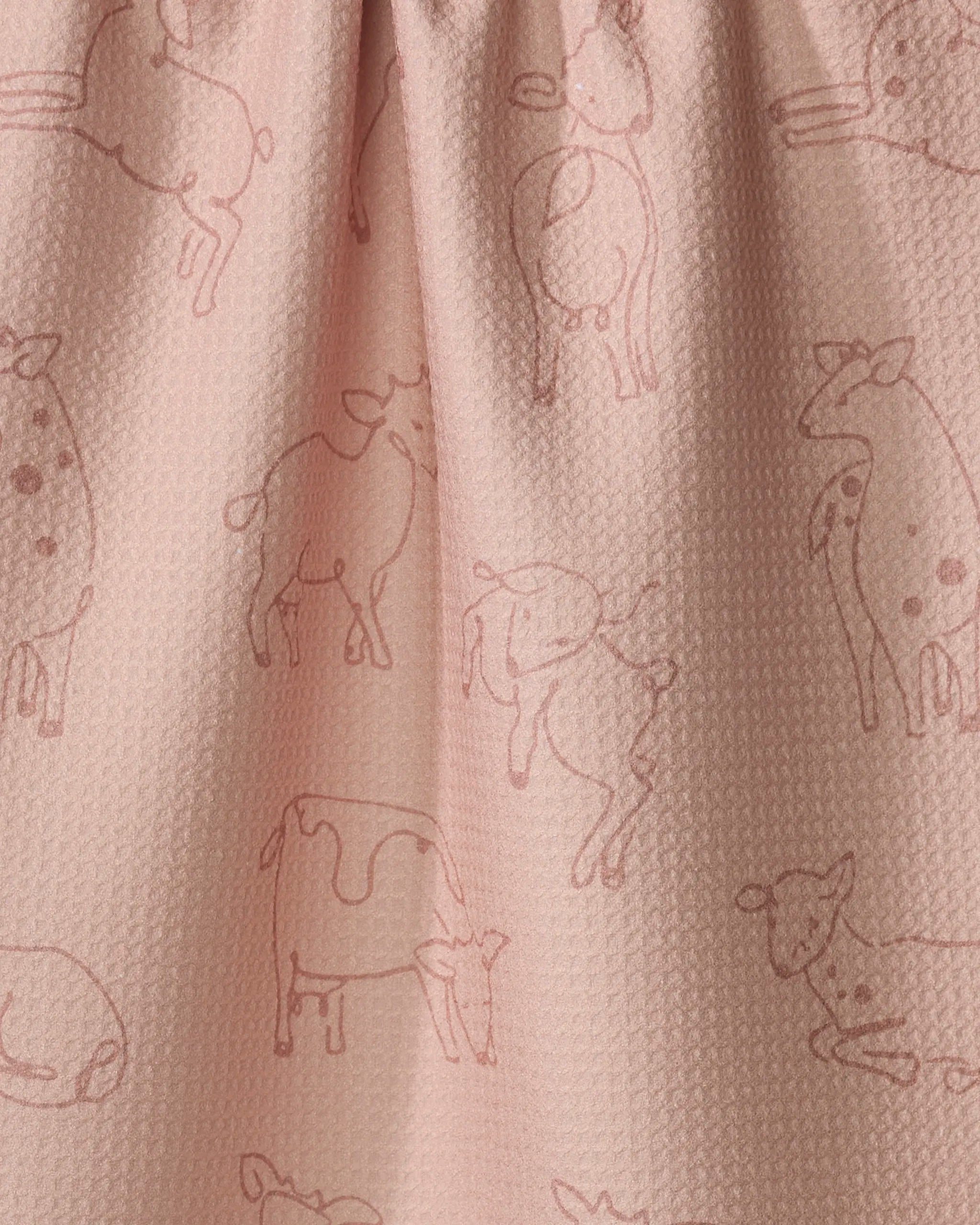 Close-up of the pink Kidding Around towel by Sara Mari—a quick-drying fabric playfully printed with simple line drawings of spotted cows in various poses, scattered across the textured material.