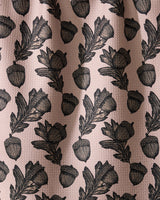 Geometry’s Kindred dish towel features an illustrated pattern of black acorns and oak leaves, evenly spaced on a textured light pink background. Ultra-absorbent fabric forms soft folds with subtle shadows and highlights.