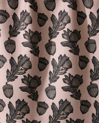 Geometry’s Kindred dish towel features an illustrated pattern of black acorns and oak leaves, evenly spaced on a textured light pink background. Ultra-absorbent fabric forms soft folds with subtle shadows and highlights.