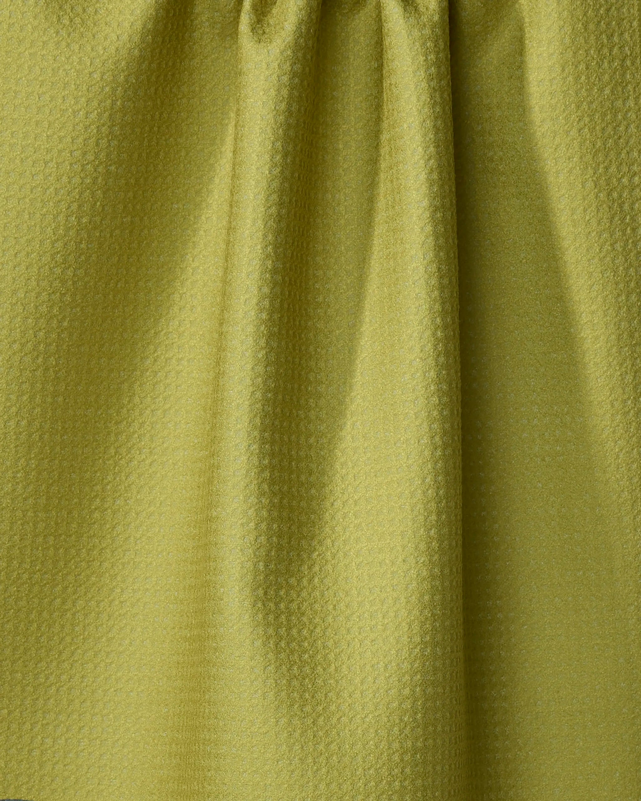 A close-up of Lizzie Clark's Kiwi Kraze tea towel, a light green recycled fabric with a subtle grid pattern and vertical folds down the center.