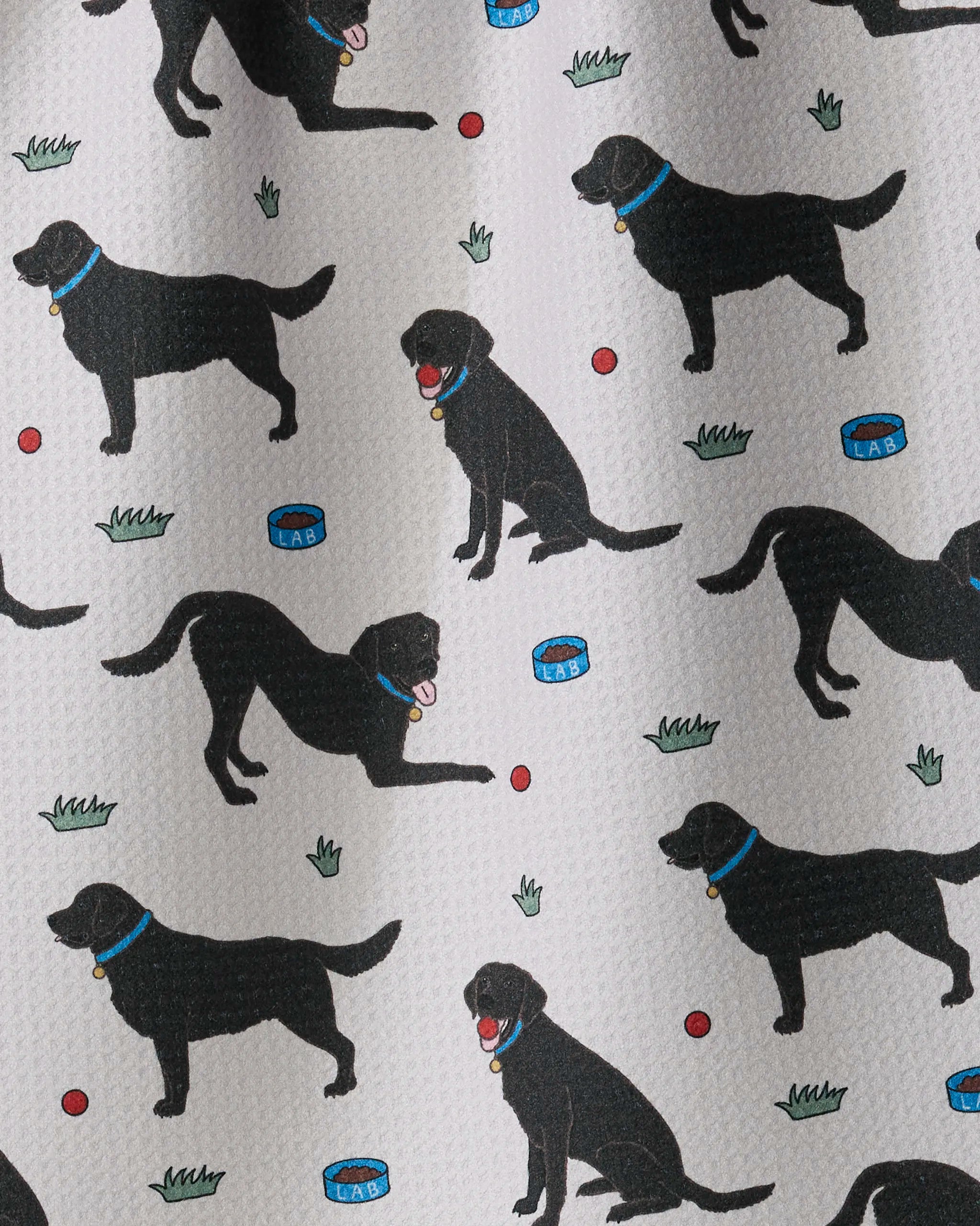 Lab Pals by Geometry features a playful pattern of black Labrador dogs in various poses with blue collars, red balls, food bowls, and small grass patches on a light background—making this ultra-absorbent tea towel a charming addition to any kitchen.