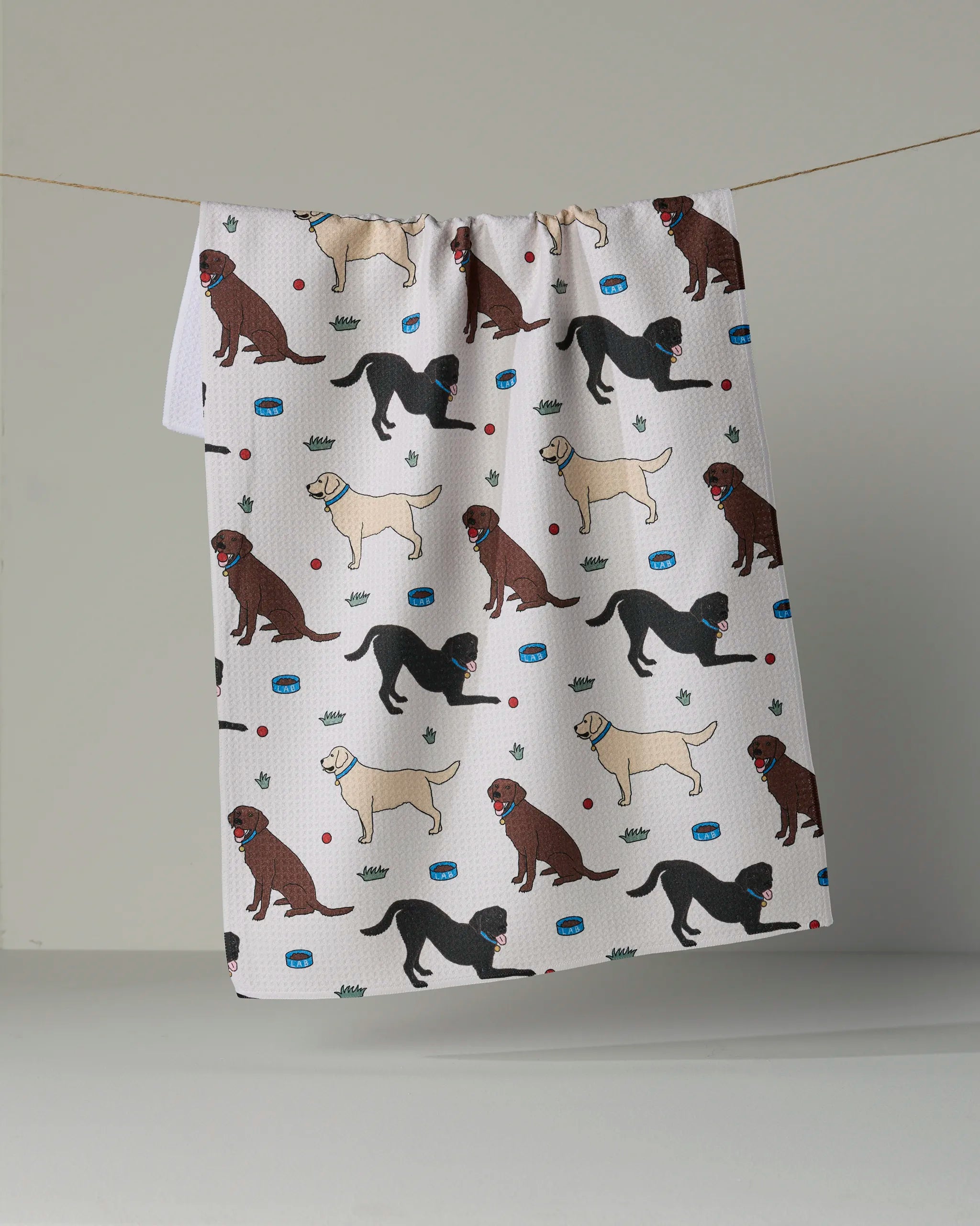 Introducing the “Lab Pals” tea towel by Geometry—an ultra-absorbent kitchen towel made from recycled materials. Featuring a lively pattern of illustrated dogs in various poses, surrounded by playful paw prints, bones, and bowls, this eco-friendly towel brings both sustainable function and whimsical charm to your kitchen decor.