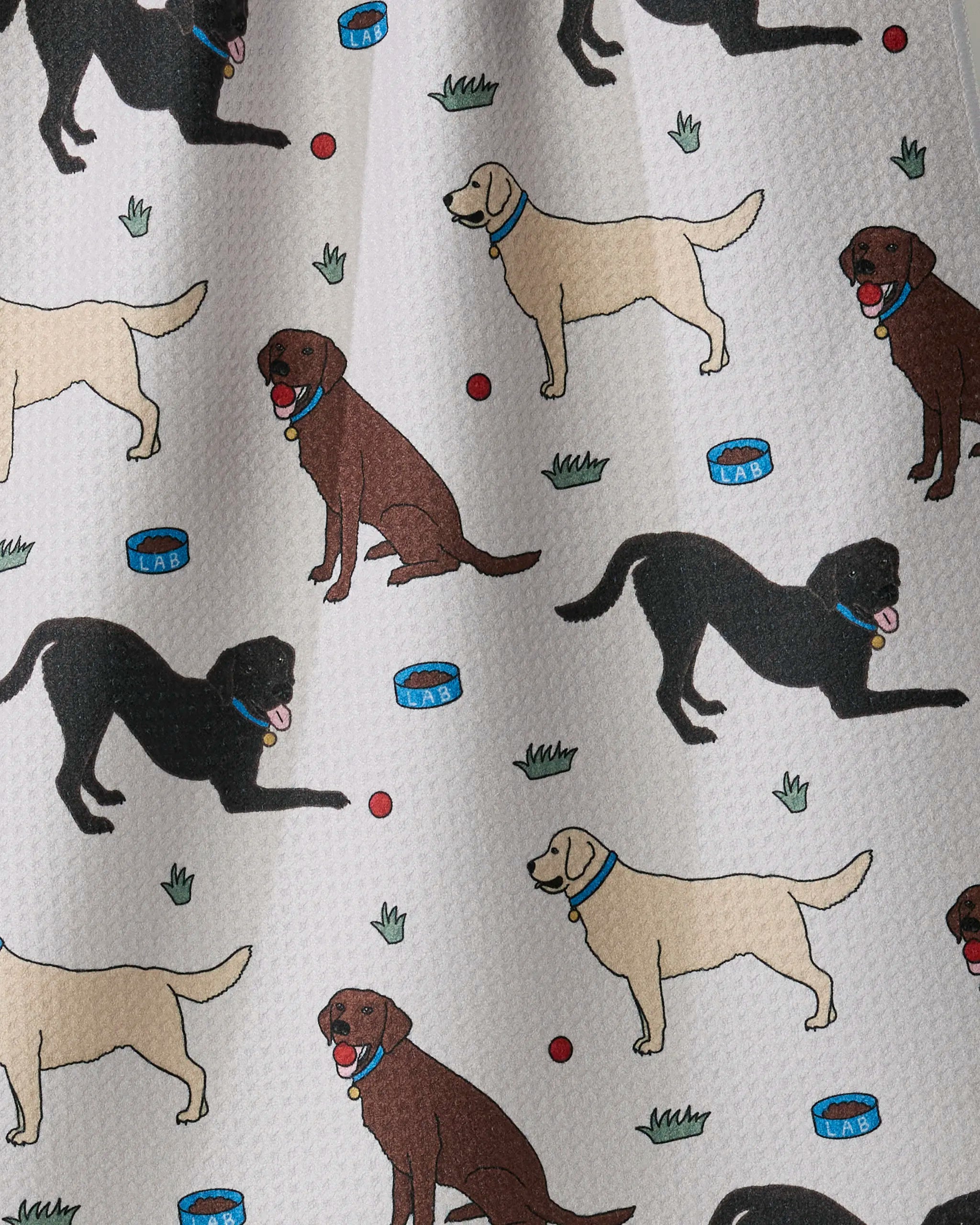Add a playful and practical touch to your kitchen with Geometry’s “Lab Pals” ultra-absorbent tea towel. Featuring a charming pattern of cartoon black, yellow, and brown Labradors romping with red balls—complete with patches of grass and blue dog bowls—this fun design pops against a crisp white textured background, making it perfect for brightening up your space while keeping things clean.