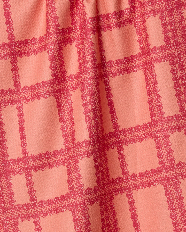 Close-up of Geometry’s Lacy Plaid fabric, featuring a pink base with a darker pink lace-like grid pattern made from recycled materials. The textured material is softly gathered at the top, forming gentle folds and shadows.