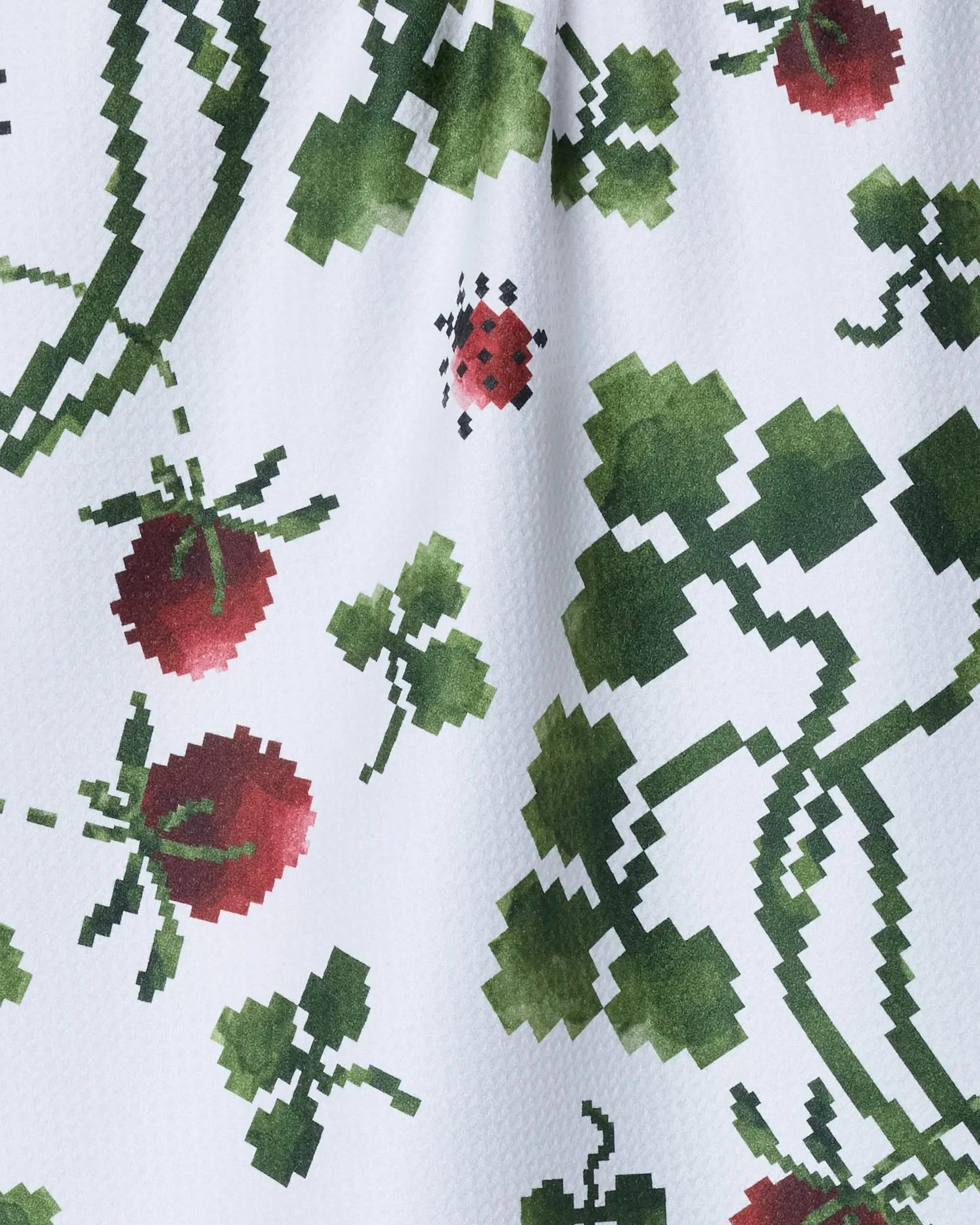 The Ladybug Fields tea towel by Geometry features a pixelated green vine, red tomato, and ladybug design on white, crafted from recycled materials for an eco-friendly touch.
