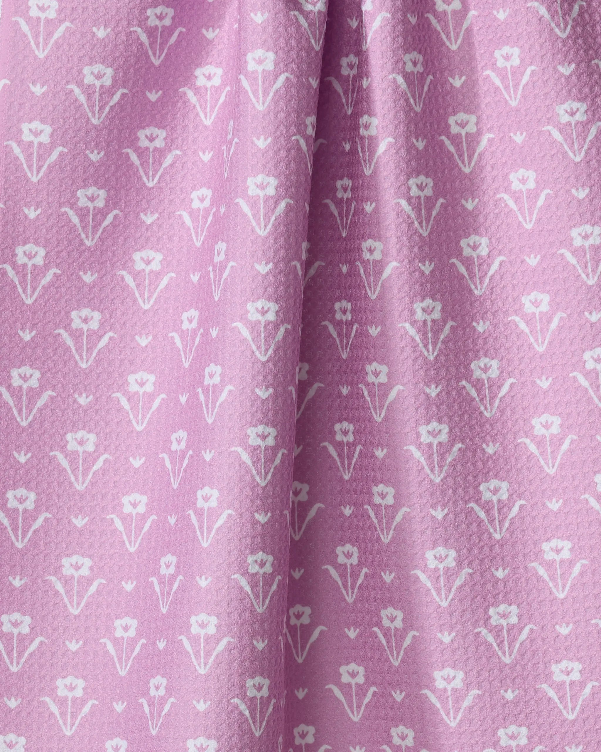 Close-up of The Buy Guide's Ladylake - Pink tea towel, made from recycled materials. It features neat rows of small white floral patterns on pink fabric with soft folds and a slightly crinkled look.