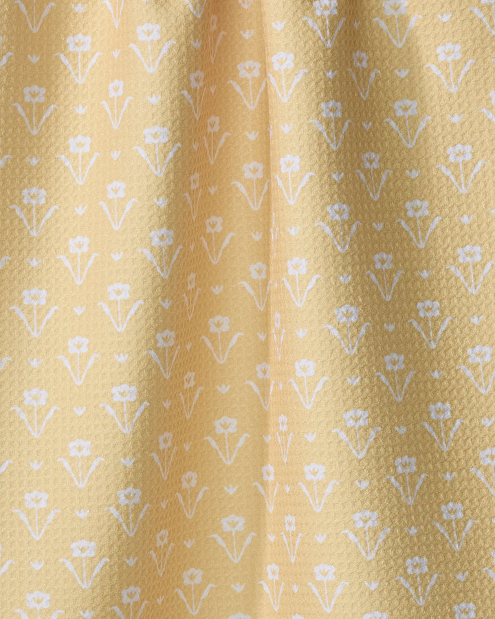 Close-up of Ladylake - Yellow by The Buy Guide: yellow fabric with a subtle textured surface, made from recycled materials, and adorned with small white flowers in neat rows—ideal for a charming kitchen towel.