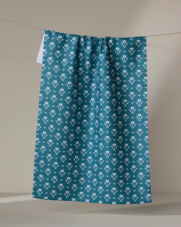 The Buy Guide’s Ladylike - Emerald tea towel, featuring a white floral pattern, hangs from a string against a neutral beige background.
