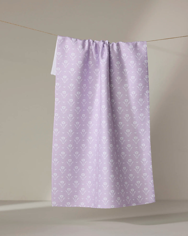 The Buy Guide's Ladylike - Lilac towel, featuring a quick-dry fabric and a subtle white floral pattern, hangs on a clothesline against a neutral backdrop.