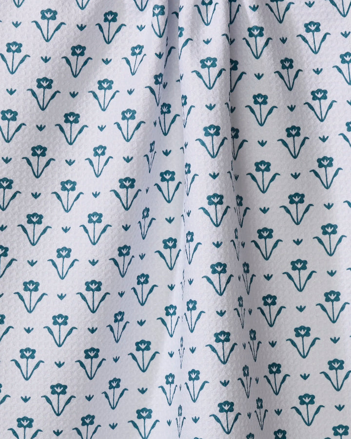 The Buy Guide’s Ladylike Too - Emerald dish towel features white fabric with a repeating pattern of small, stylized blue floral designs arranged in neat rows, plus a slight vertical fold near the center.