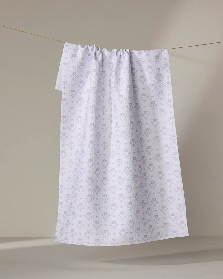 The Buy Guide's Ladylike Too - Lilac tea towel, featuring a subtle lilac floral pattern, hangs on a clothesline against a neutral beige background.