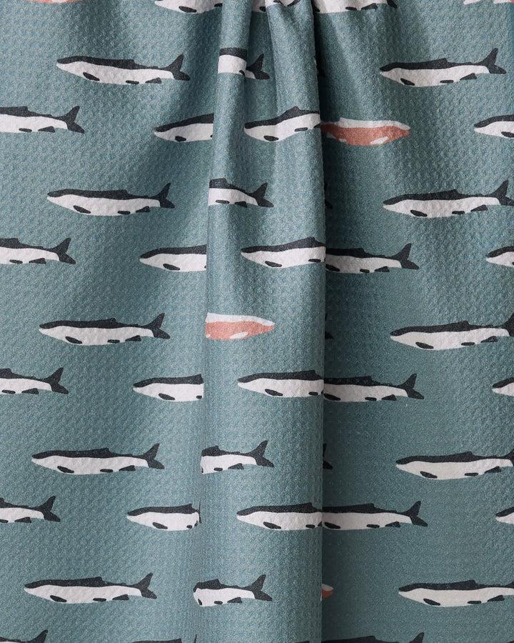 Coit Creative’s “Lake Fish” tea towel features rows of stylized black and white fish swimming on teal, with one standout fish marked in pinkish-orange. Made from recycled materials, it's a sustainable and eye-catching kitchen accessory.