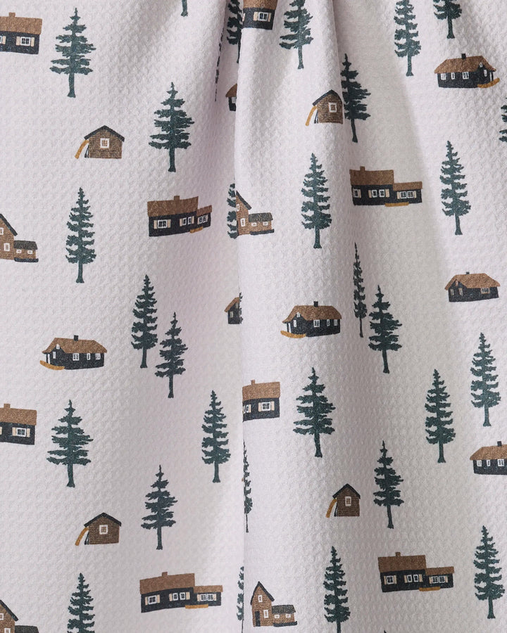 The Lakehouse Cabins kitchen towel by Coit Creative features white textured fabric with green pine trees and brown cabins, offering an ultra-absorbent and stylish addition to your kitchen.