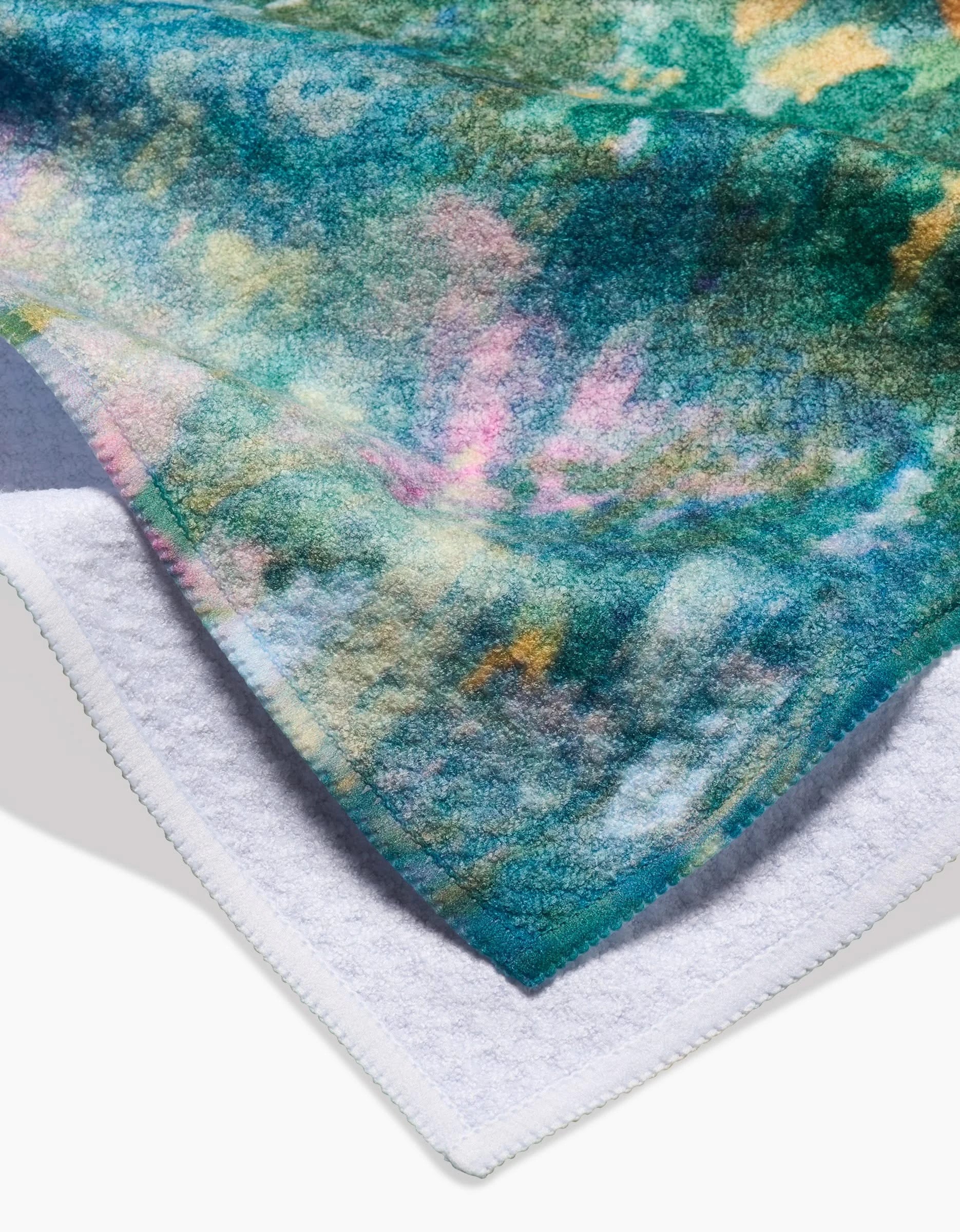 A close-up of Taryn Brennan’s Land of Milk and Honey Kitchen Tea Towel displays a vibrant abstract pattern in green, blue, pink, and yellow on the front with plain white Geoweave fabric on the back.