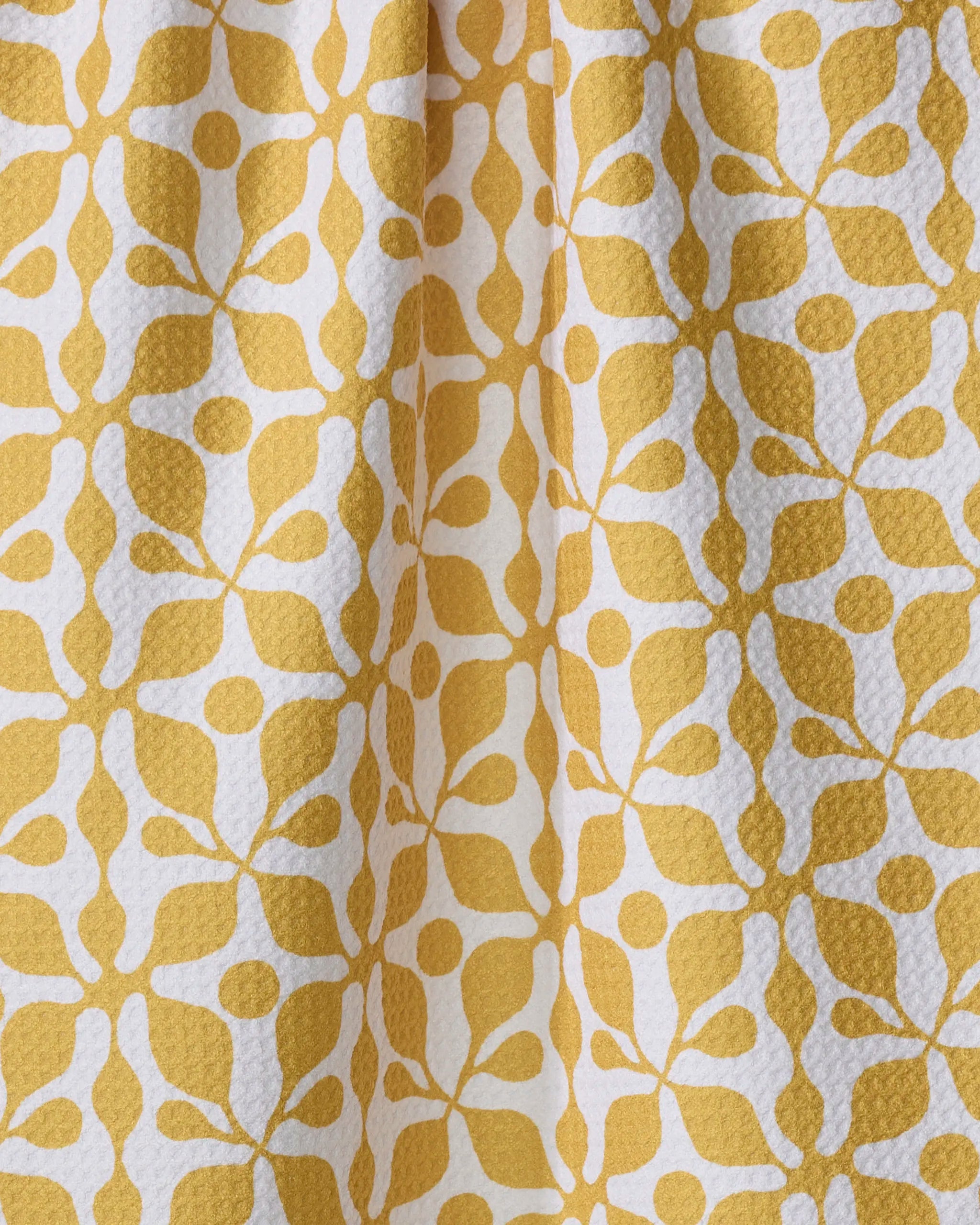 Renee Fly's "Lattice" dish towel features a yellow and white pattern with a repeating floral or leaf design and a subtly textured, dimpled surface, shown draped in gentle folds.