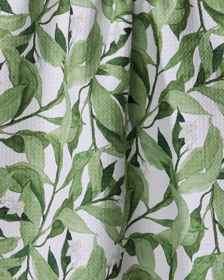 A close-up of Aubrey Fairchild's Leaf It To Me dish towel, ultra-absorbent with a textured surface, showcases a green leafy botanical pattern and small white flowers on a white background.