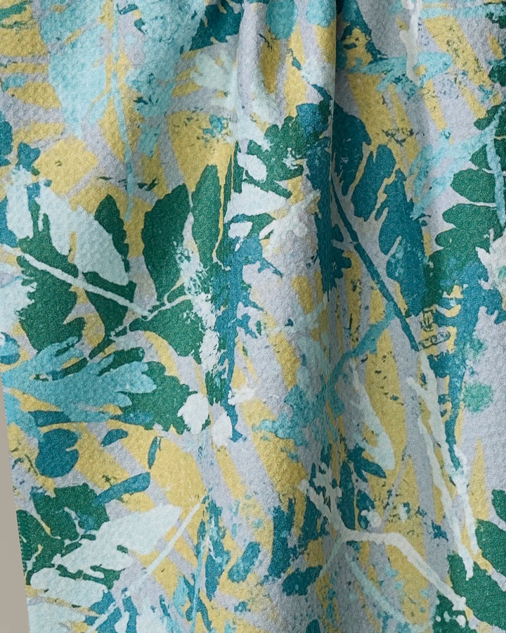A close-up of the Taryn Brennan Leafy Bush tea towel, showcasing an ultra-absorbent design with overlapping green, blue, and yellow leafy patterns on a light background for an abstract, nature-inspired look.