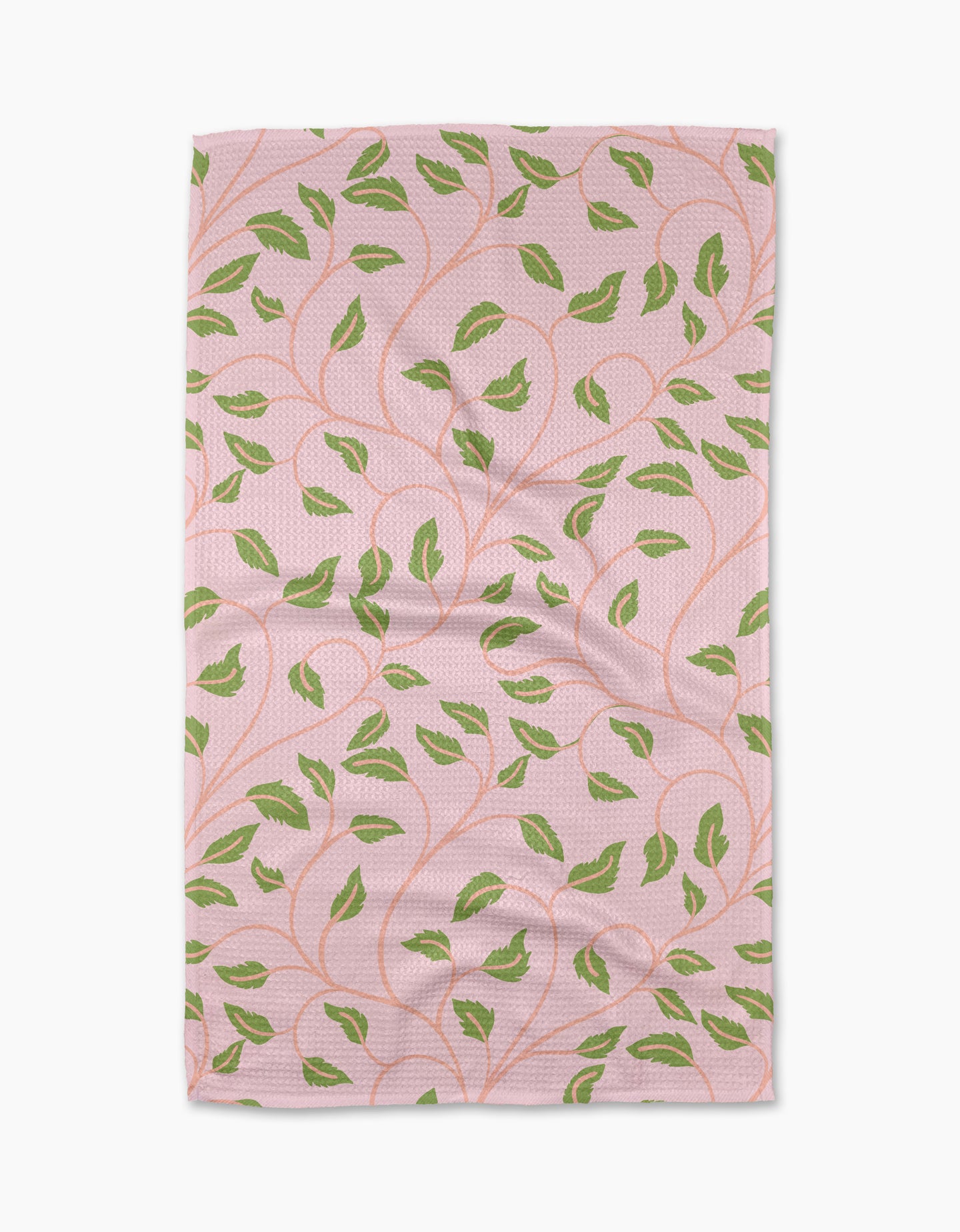 The Leafy Maze kitchen towel by Jasmine Blooms Designs is a rectangular pink recycled towel featuring green leaf patterns and winding orange stems, shown laid flat with some visible creases.