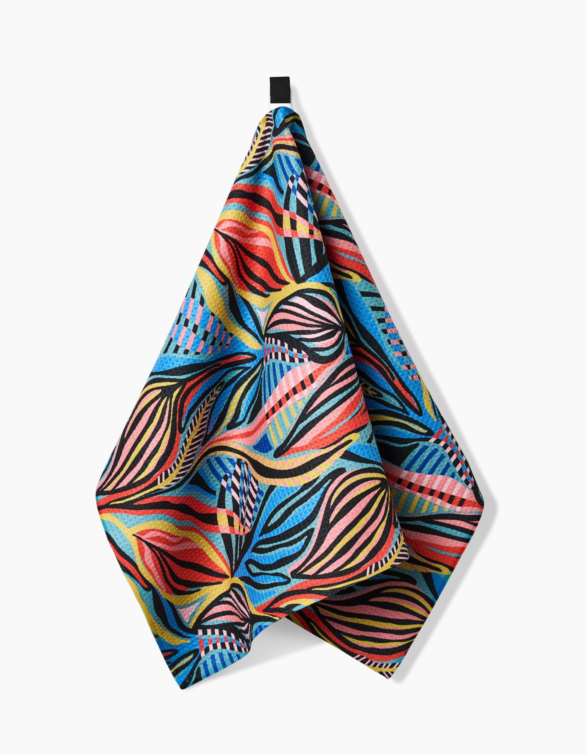 The Leafy Path Tea Towel by Masha Volnova features a bold, abstract pattern in red, blue, yellow, black, and pink on Geoweave fabric. It hangs from a black loop against a white background.