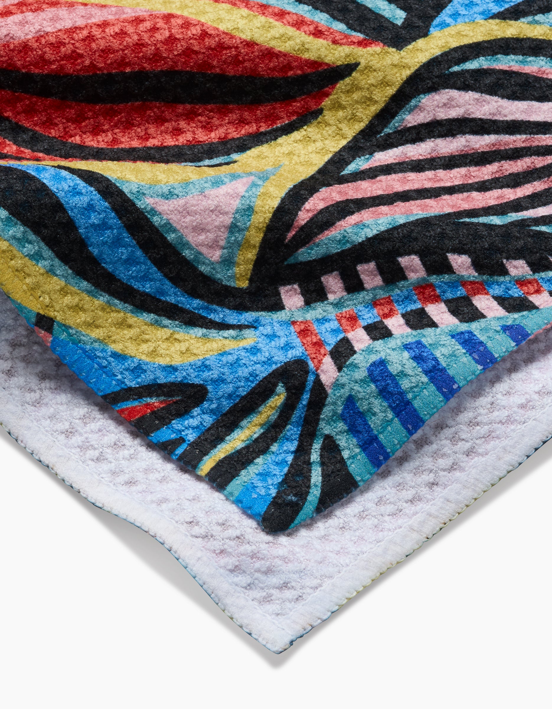 A close-up of the Leafy Path tea towel by Masha Volnova, featuring colorful abstract patterns in red, yellow, blue, pink, and black on Geoweave fabric layered over a white textured background.