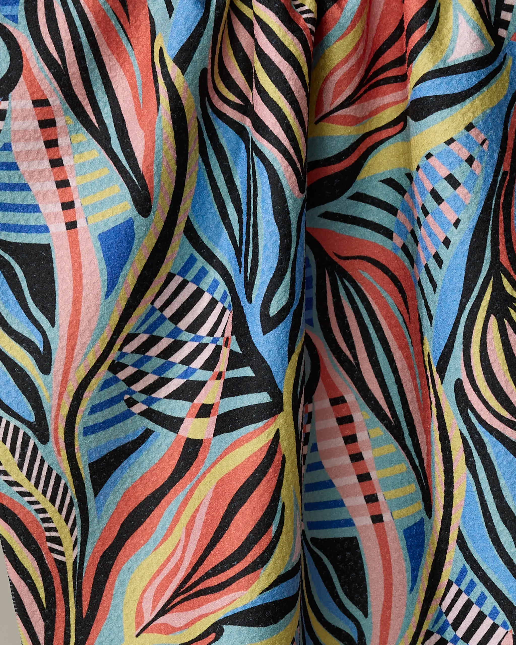 A close-up of Leafy Path by Masha Volnova, a recycled kitchen towel with wavy lines and leaf-like shapes in blue, pink, yellow, black, and orange—striped and solid sections create a vibrant abstract pattern.