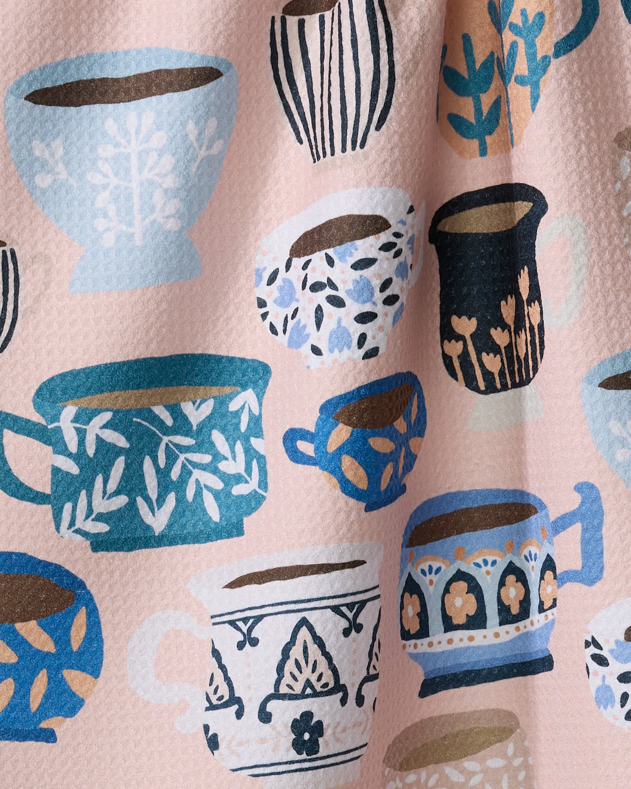 Les Tasses by Cottonflower Studio features blue, white, and brown cups with floral and leaf patterns on a textured light pink backdrop—an ideal design for ultra-absorbent kitchen tea towels.