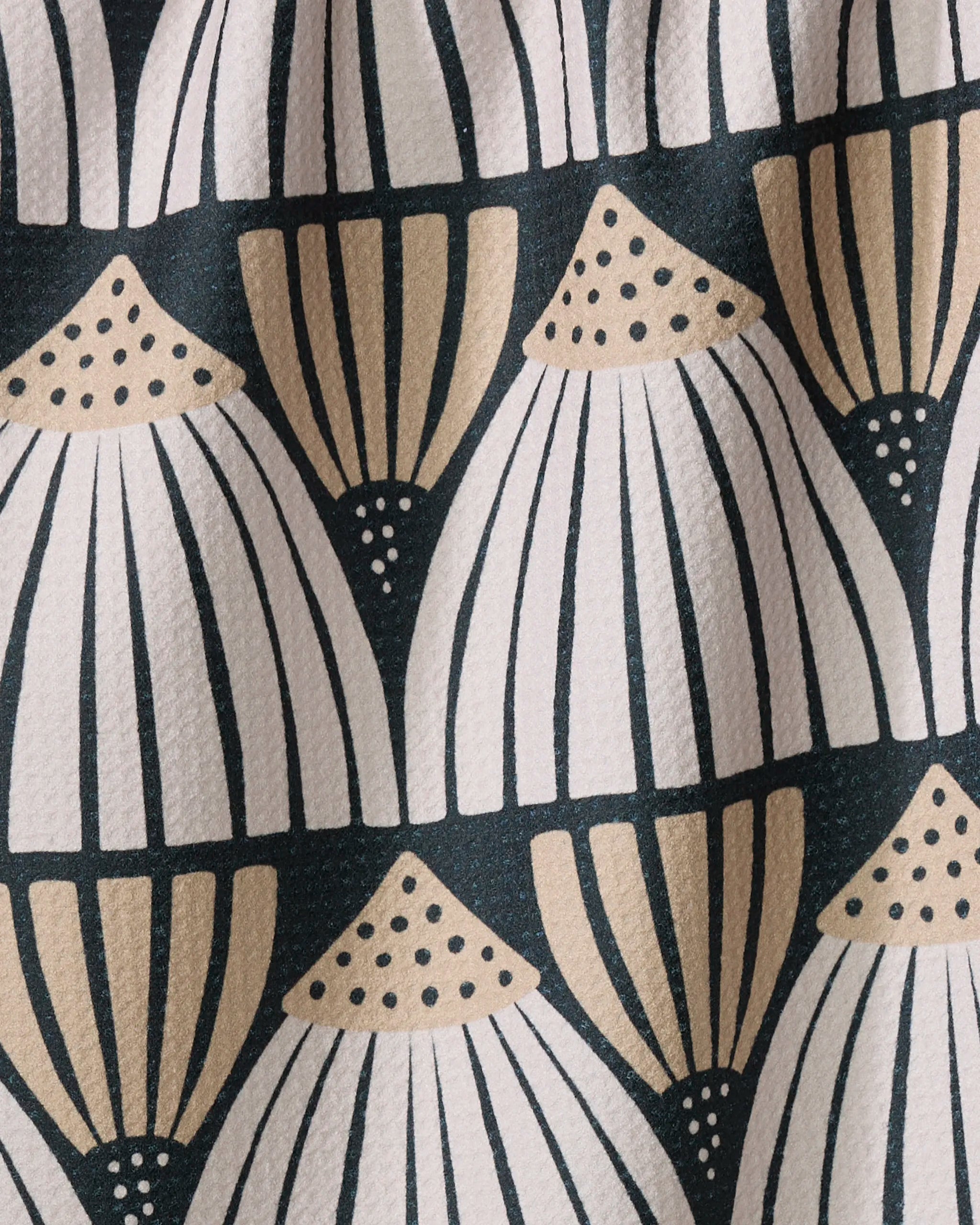 A close-up of the Letitia dish towel by Amy MacCready, featuring an absorbent fabric with a repeating geometric fan or shell pattern in beige, white, and black, detailed with dotted tops and vertical lines.