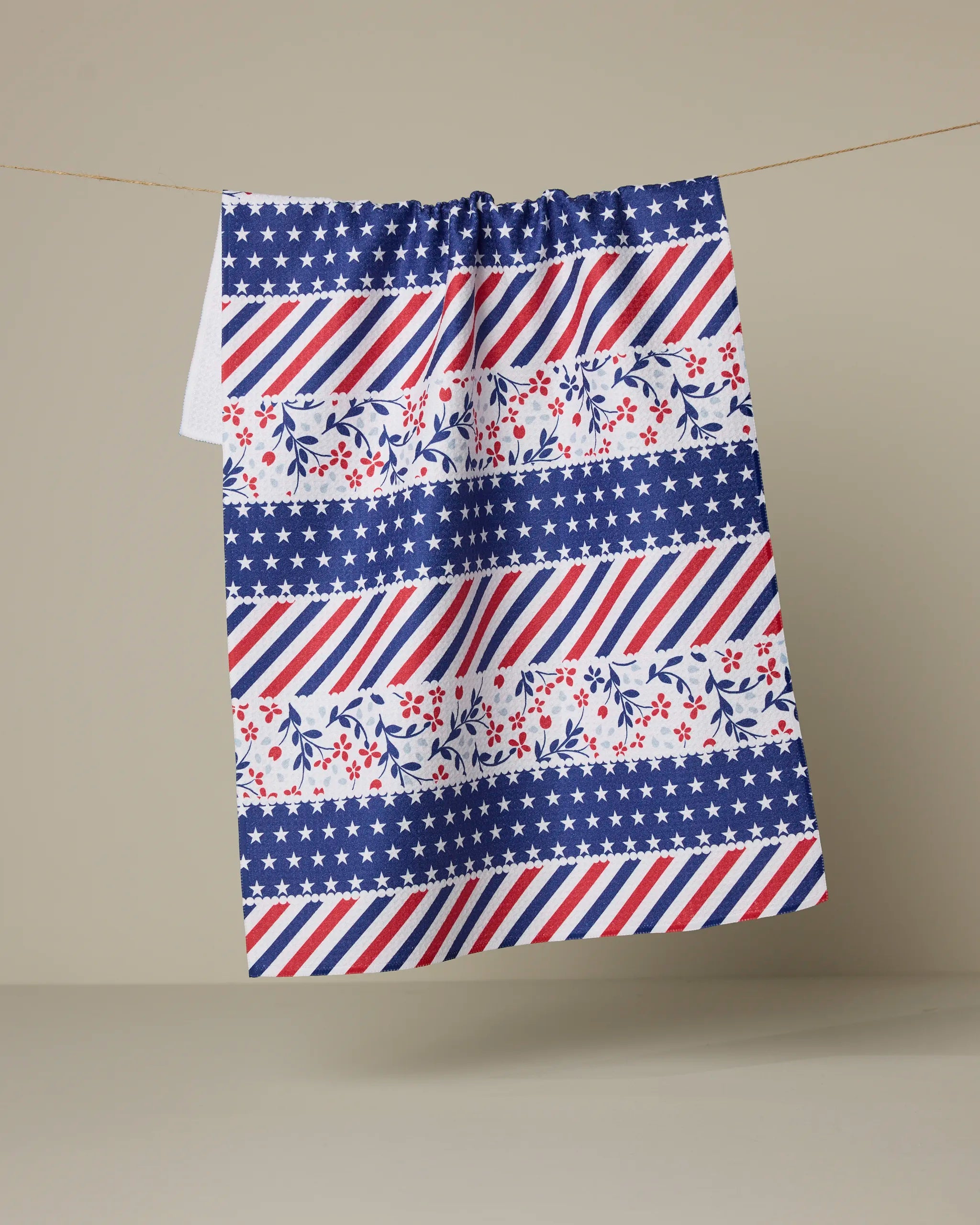 The Liberty Ribbon tea towel by Geometry features blue and white stars, red and blue stripes, and red and blue floral patterns—an absorbent dish towel that adds charm to any kitchen.