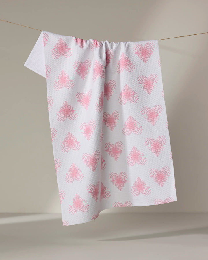 The Hufton Studio Life Line Hearts towel, featuring pink heart patterns on a quick-drying white fabric, is draped over a clothesline against a neutral background.