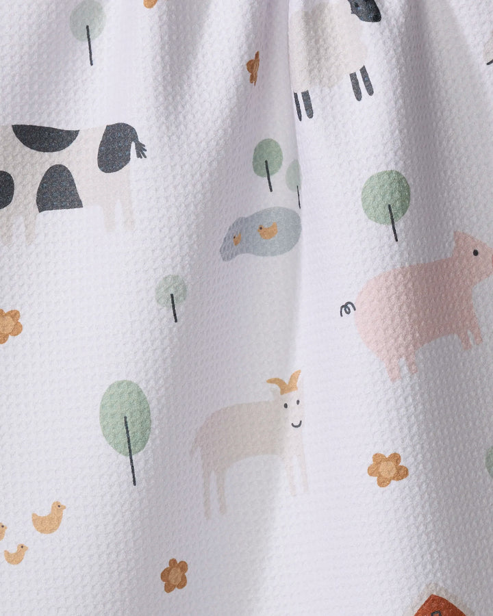 The Coit Creative Light Farm Animals kitchen towel features a white textured fabric adorned with pastel illustrations of cows, pigs, goats, sheep, chickens, trees, and yellow flowers. Made from recycled materials for an eco-friendly touch.