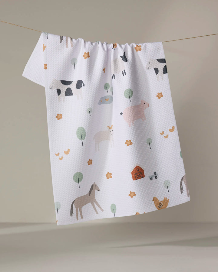 The Coit Creative "Light Farm Animals" tea towel, made from recycled materials and featuring farm animal illustrations, hangs textured and white against a neutral background.