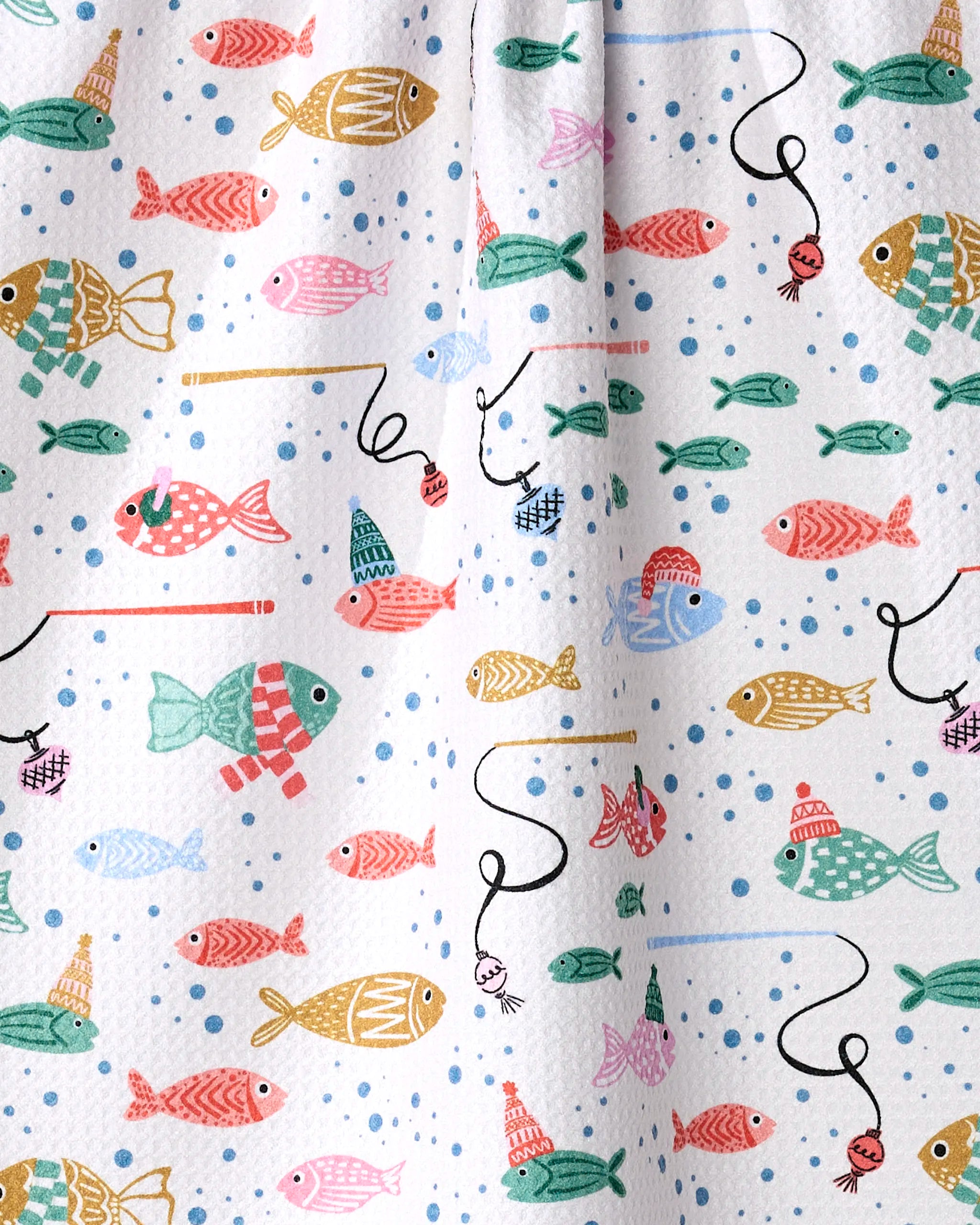 The "Light Holiday Fish" kitchen towel by Charlie Rowan Designs features colorful fish in hats and bobbers on a white, blue-dotted background for a whimsical touch, and is crafted from recycled materials.