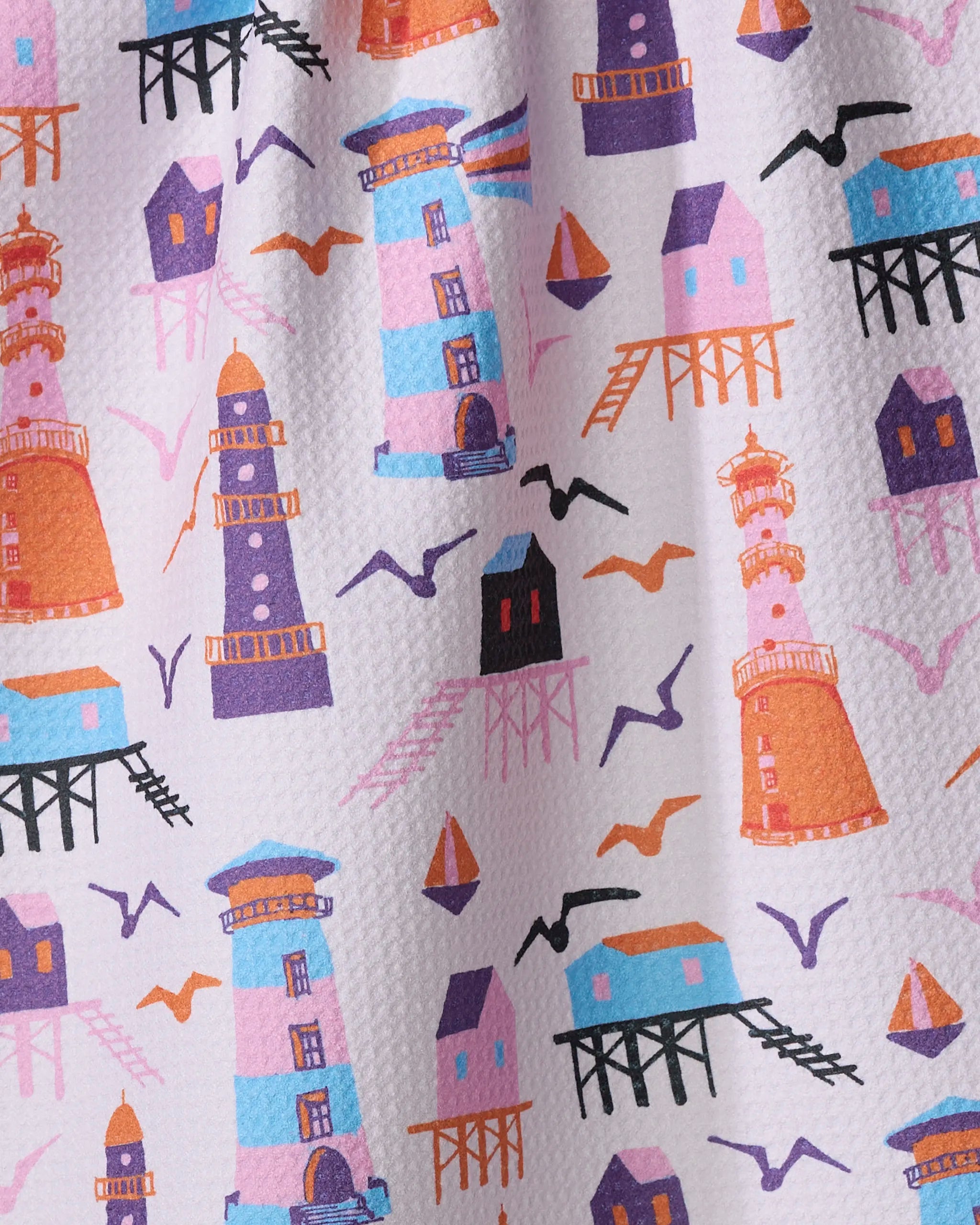 Lighthouse In Pink by Ania Zwara Art: a patterned kitchen towel with colorful illustrations of lighthouses, stilt houses, sailboats, and birds on white textured fabric. Made from recycled materials in vibrant orange, blue, purple, and pink.