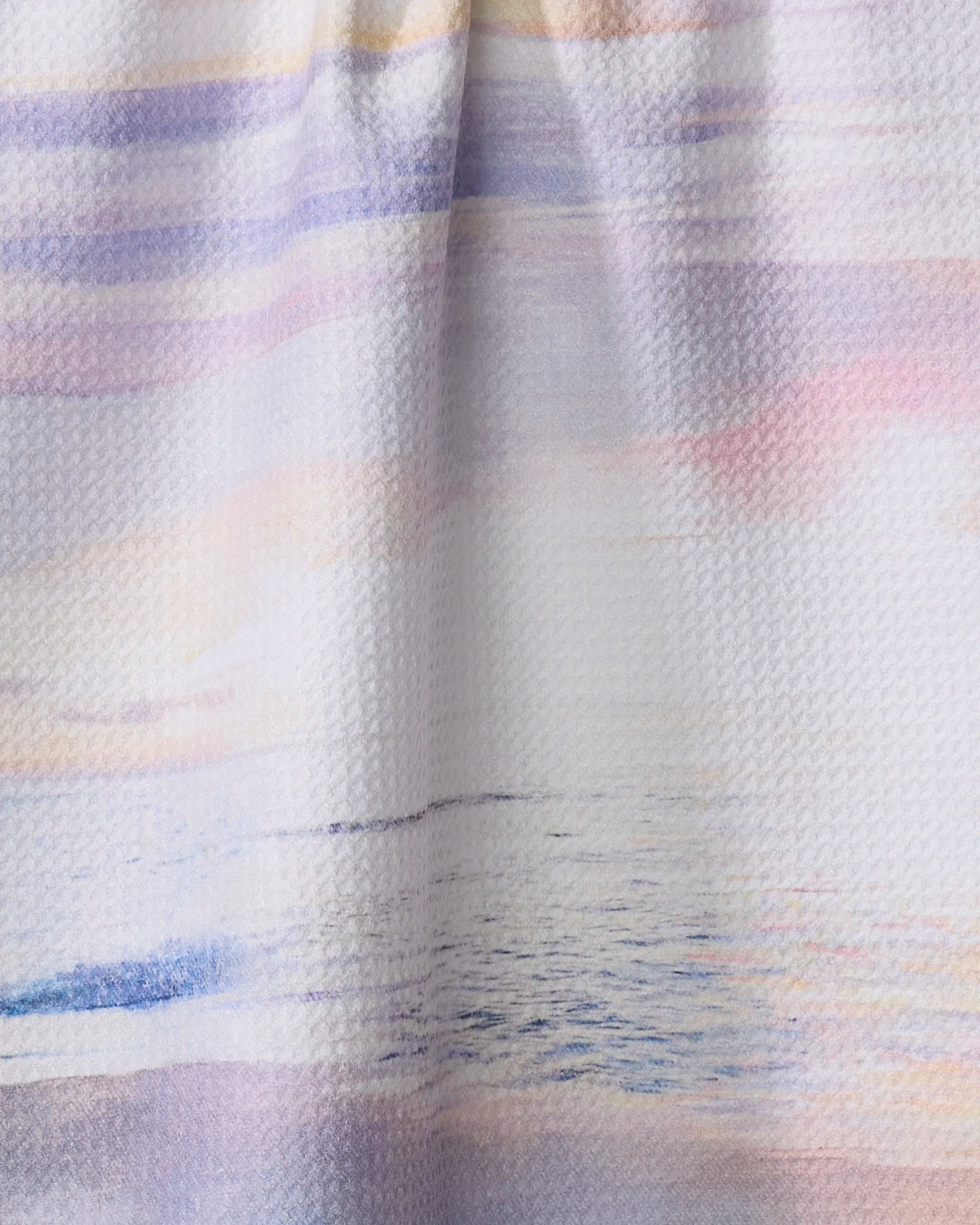 A close-up of Stefanie Bales' Lilac Coast towel reveals a serene, pastel watercolor design with soft pink, purple, blue, and yellow streaks—ideal for a stylish, quick-drying accessory.