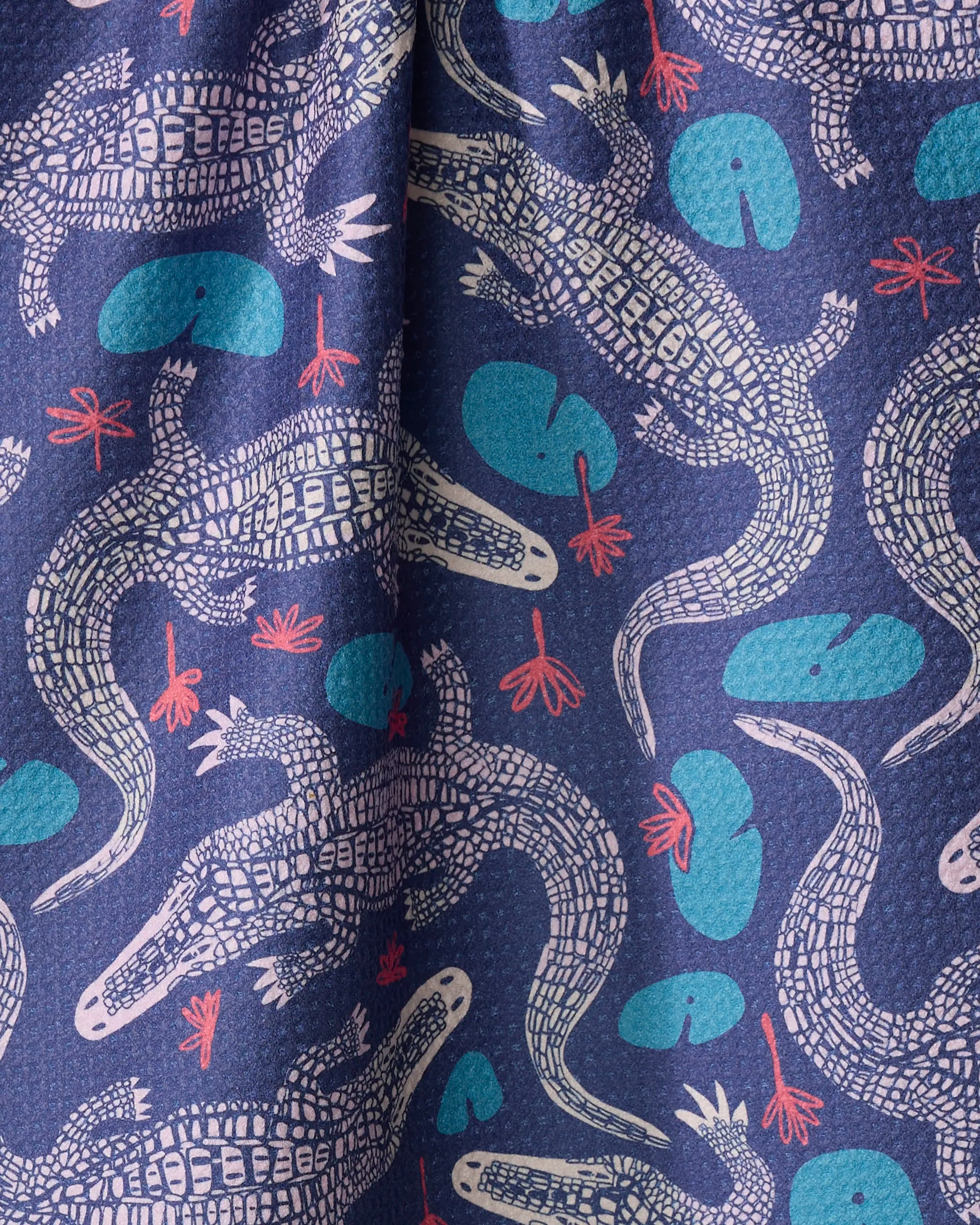 The Elisabeth Wing Lillygator kitchen towel features illustrated crocodiles, blue lily pads, and pink water plants on dark blue, crafted from recycled materials.