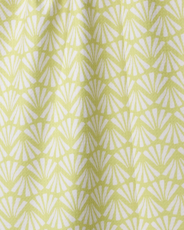 The Lime Blossom kitchen towel by Geometry features a repeating white fan or shell pattern on light green, creating a geometric and textured look. Made from recycled materials, the soft fabric drapes gently.