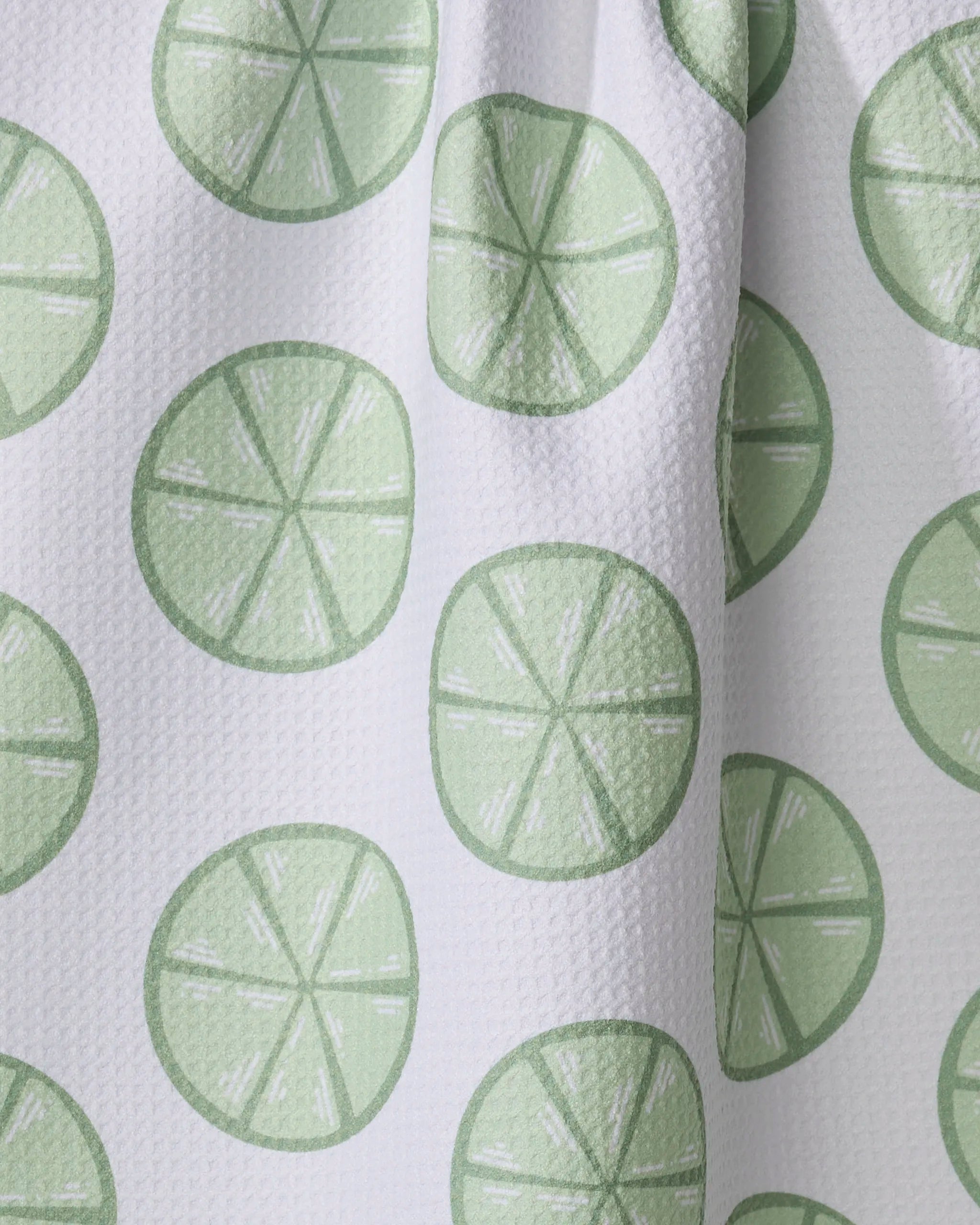 Lime Doodles by Letters By Shells is an eco-friendly tea towel featuring white textured fabric with a repeating pattern of light green lime slices, each with eight segments—perfect for brightening up your kitchen.