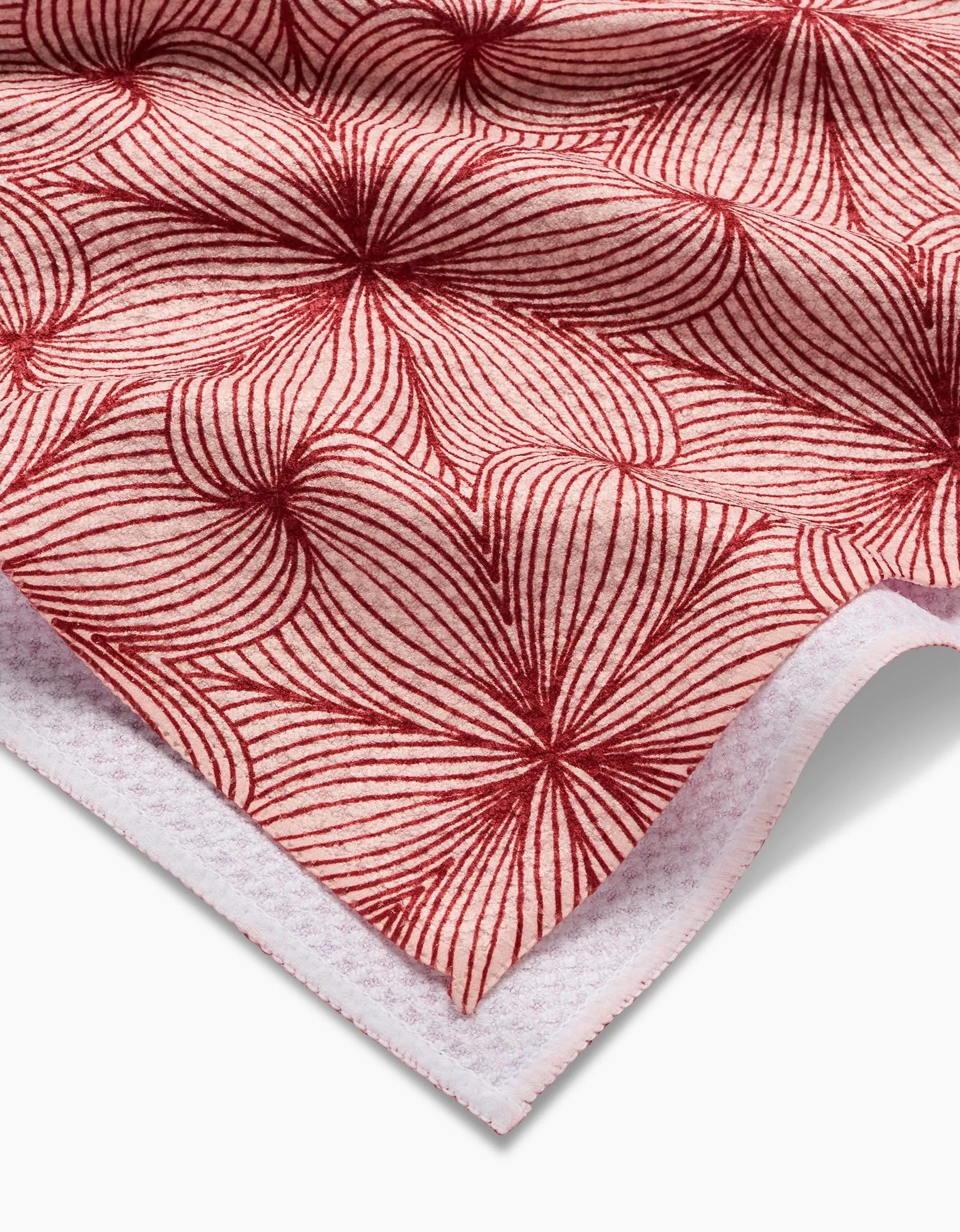 The “Lined” towel by Marta Harvey features a red floral pattern of radiating lines on white fabric. Ultra-absorbent and soft with slight texture, it’s shown close-up with a folded corner revealing the reverse side.